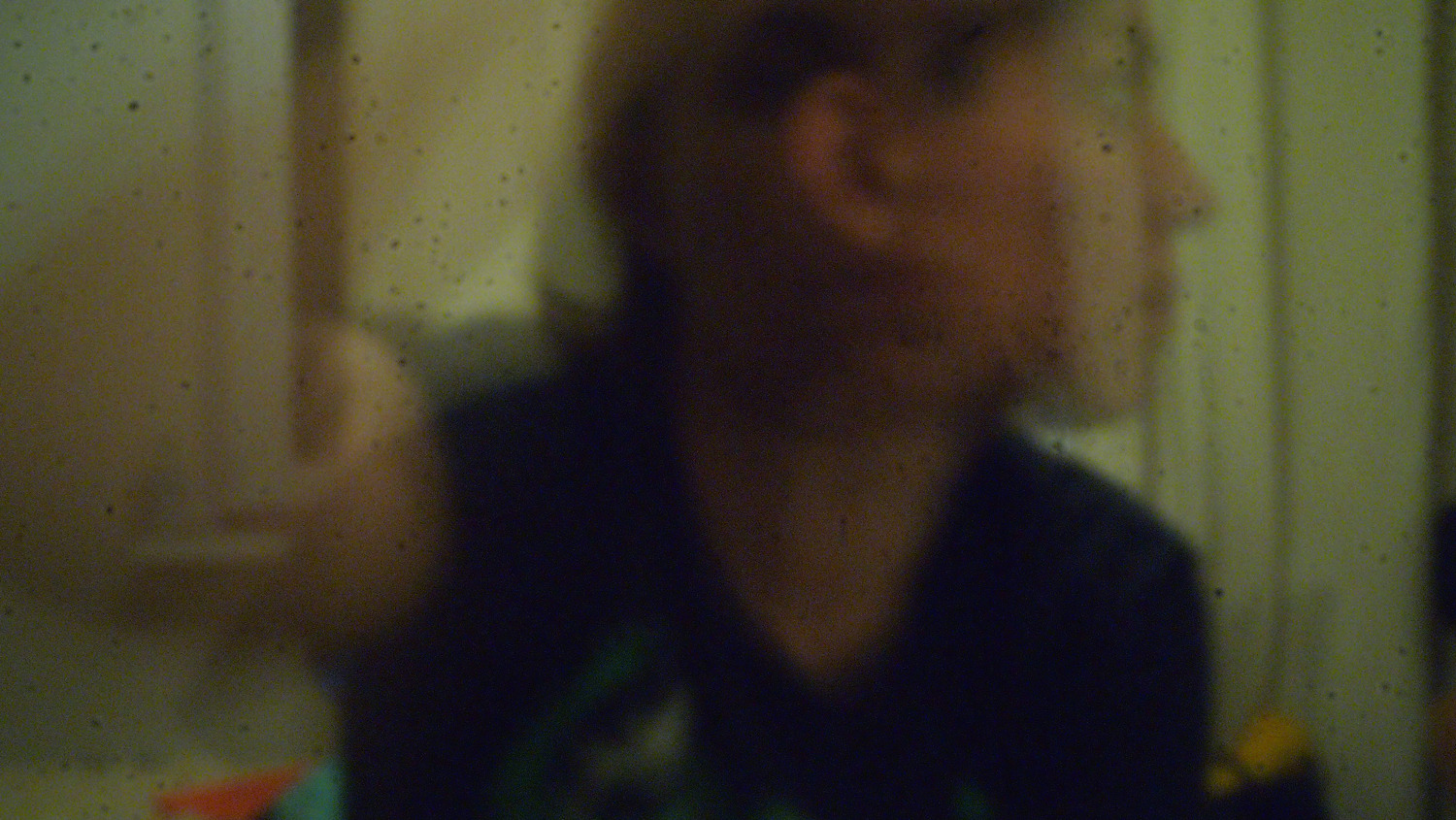 A blurry, low-light profile of a person viewed through a grainy, textured surface.