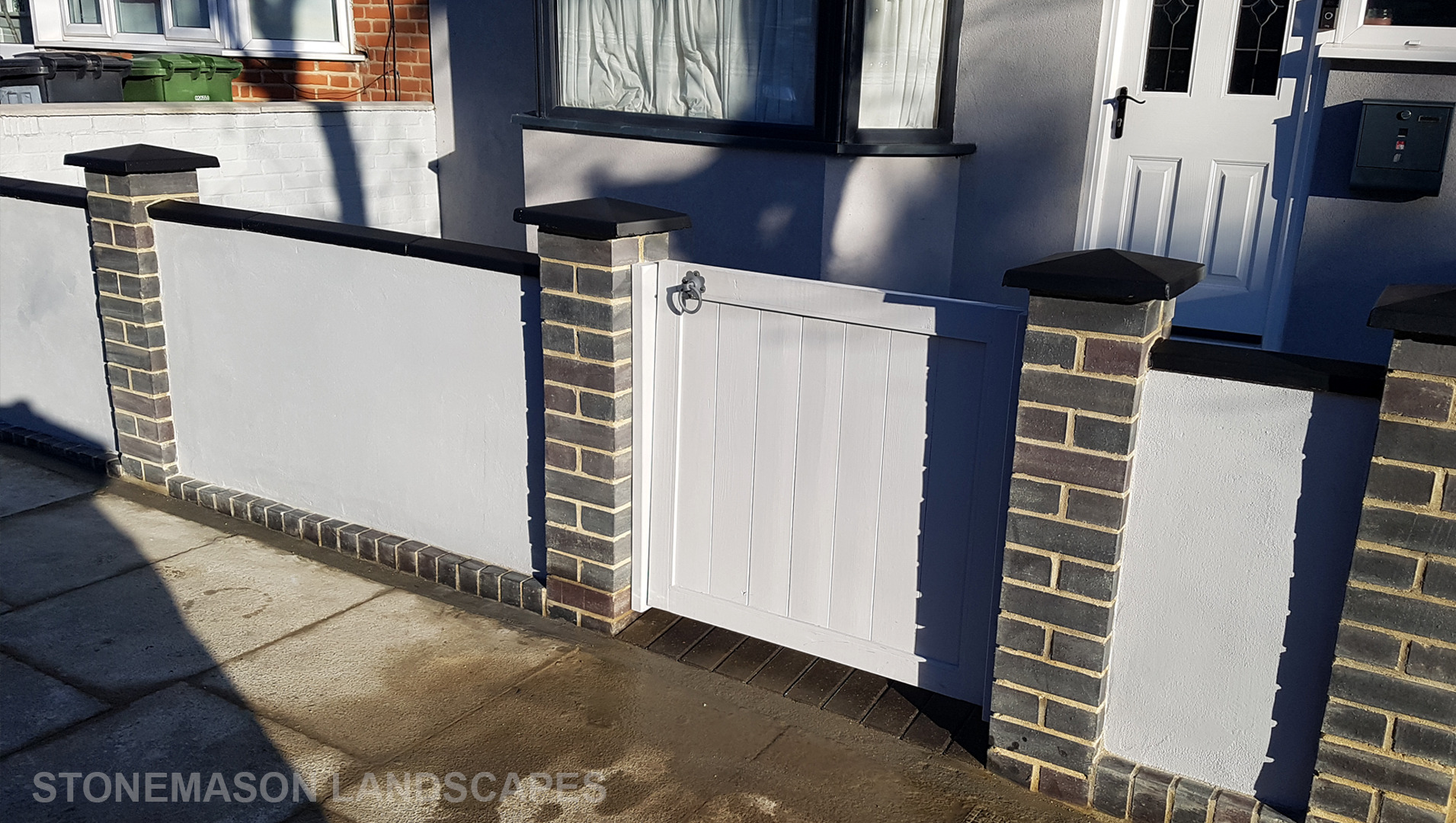 Blue perfurated brick wall with black coping and caps and grey rendering