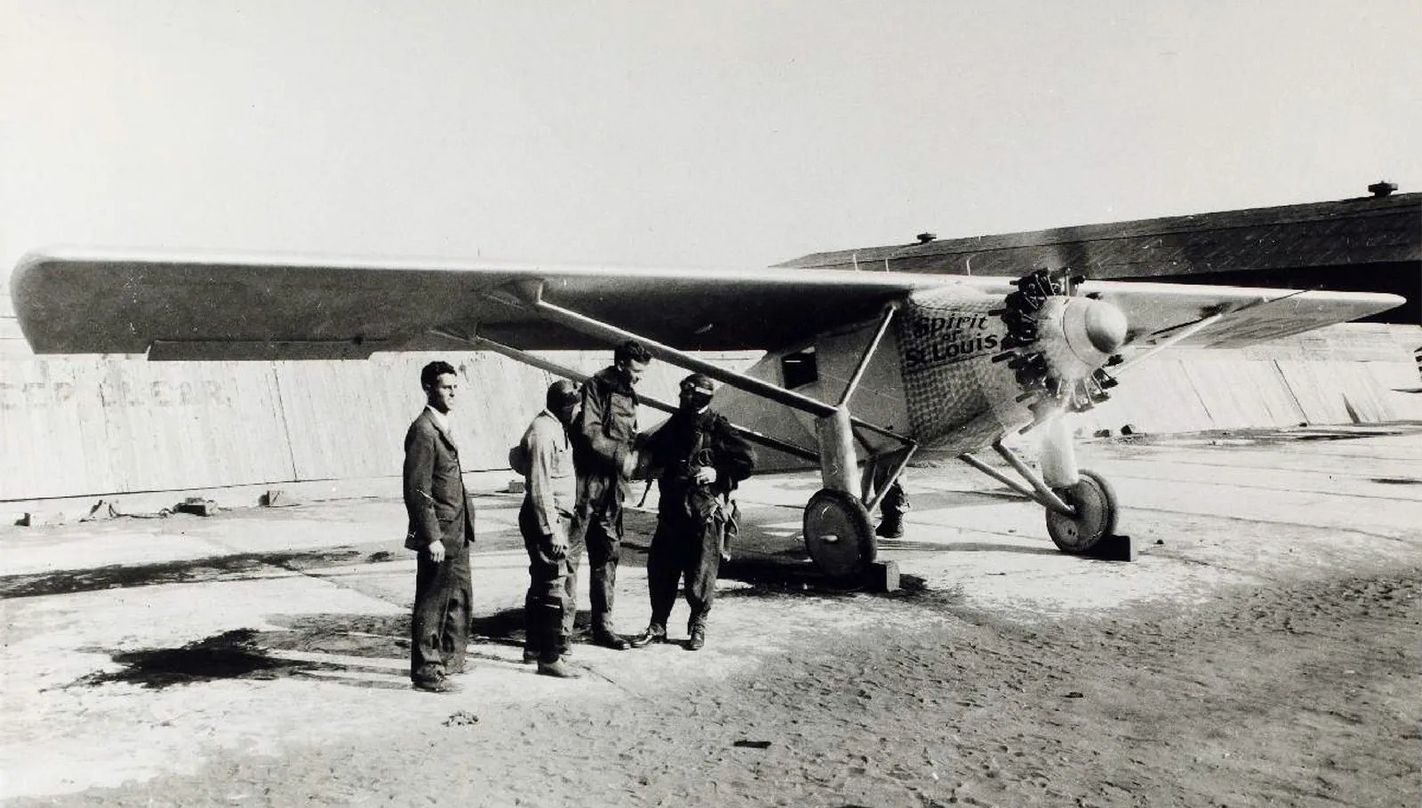 Charles Lindbergh and crew stand beside the historic Spirit of St. Louis aircraft on a runway.