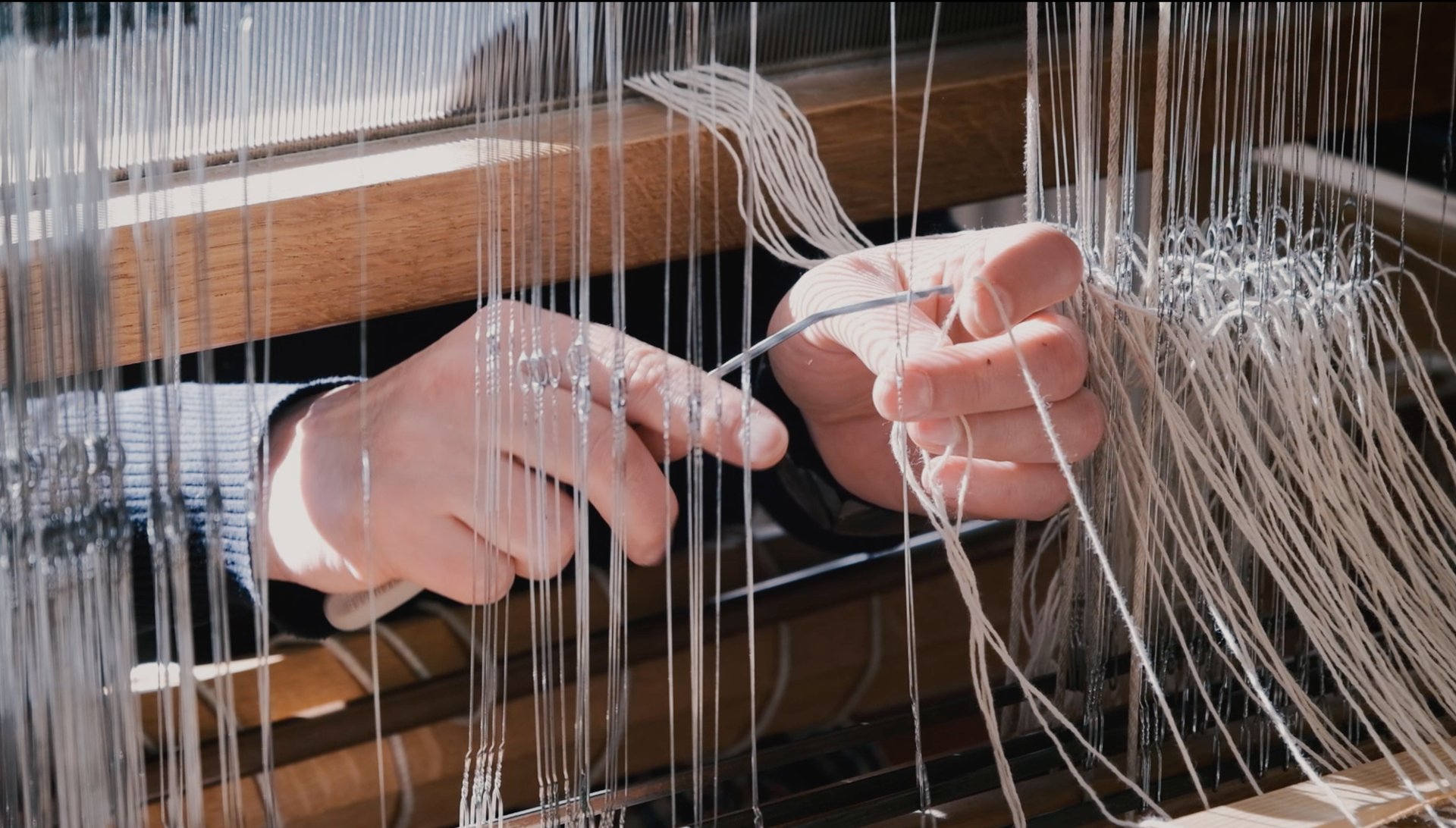 A person inserts the warp threads through metal eyelets of the harnesses