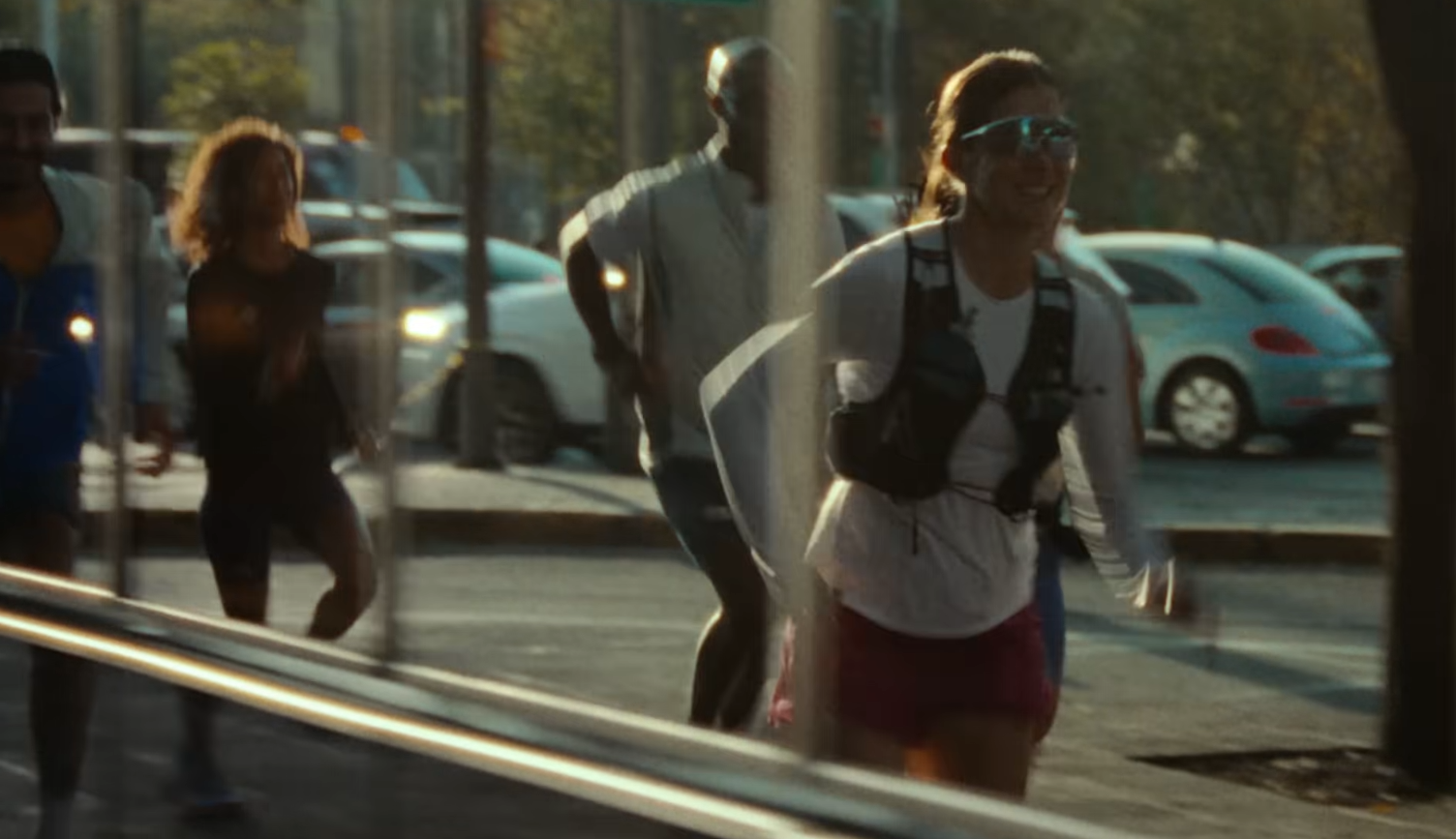 Athletic woman wearing a hydration vest and sunglasses running on a city street with other runners.
