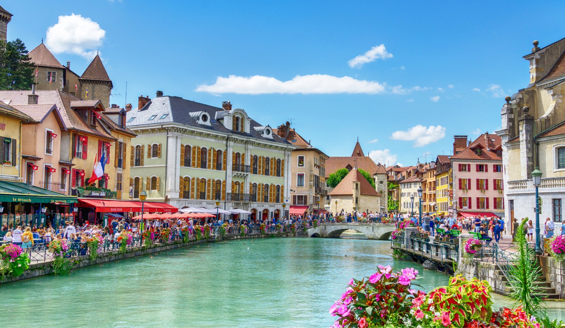 Scenic view of Annecy canal with colorful buildings, outdoor cafes, and a stone bridge in the French Alps.