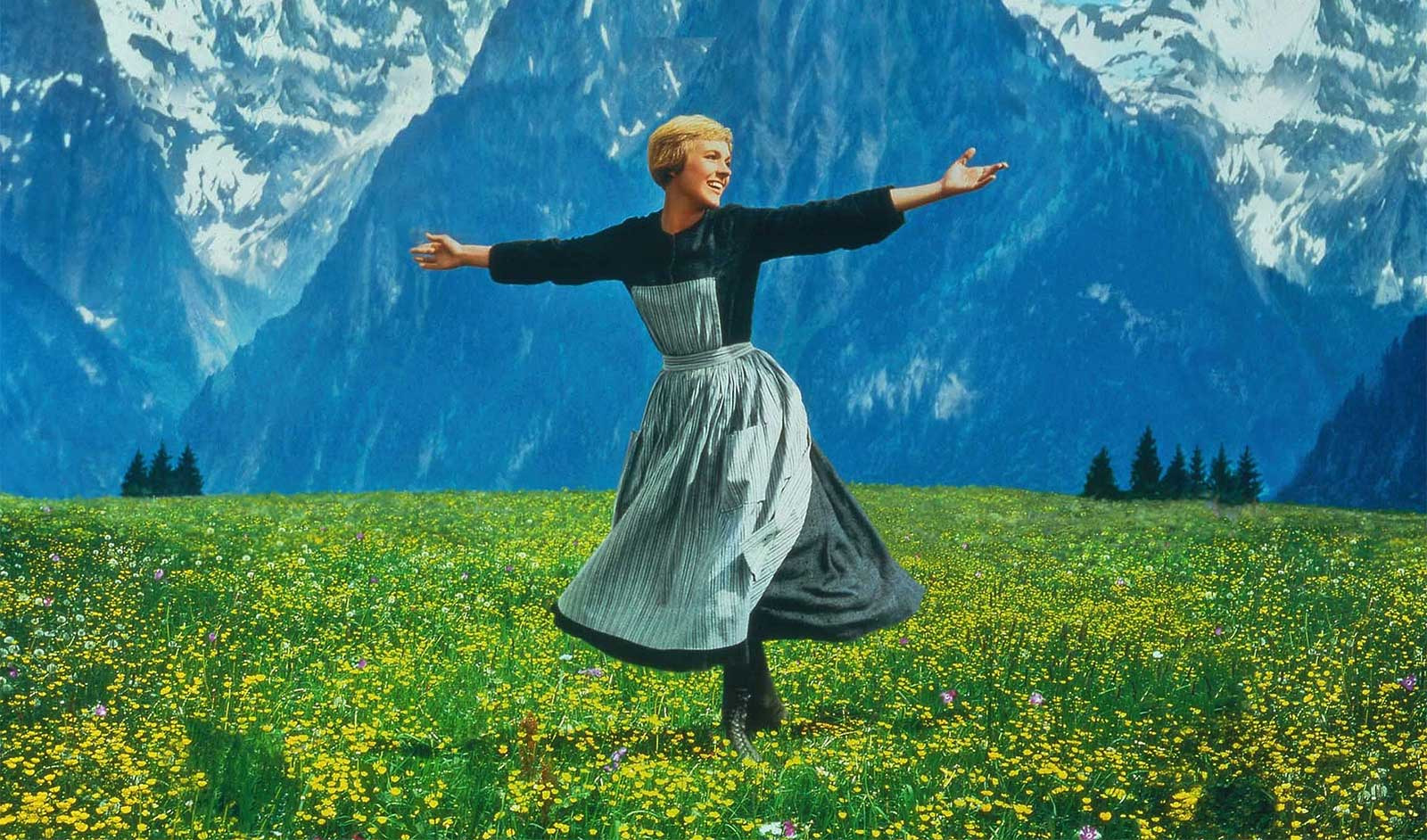 Julie Andrews as Maria stands arms wide on a mountain in The Sound of Music