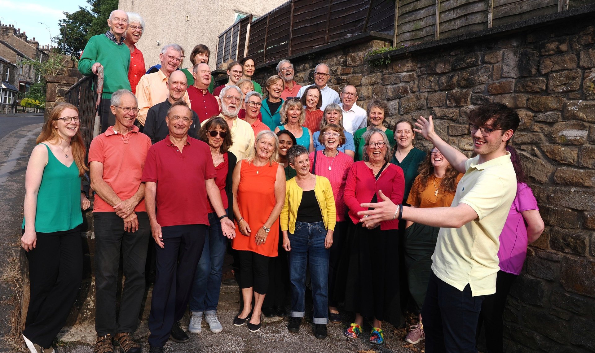 The choir singing outside wearing bright coloured tops