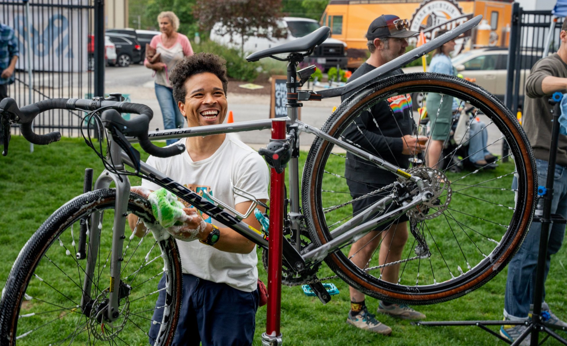 A young man smiling and washing a bike held high on a stand