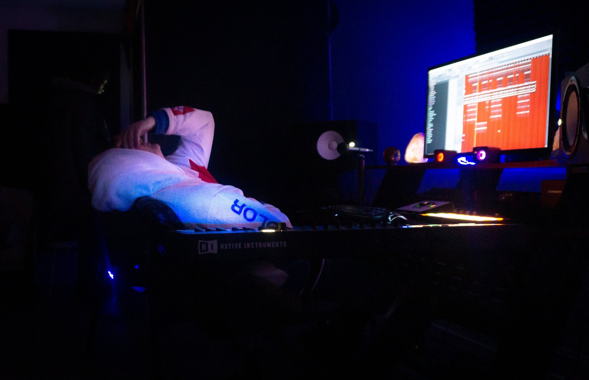 a man is slumped over in a chair in the dark. With a computer screen on.