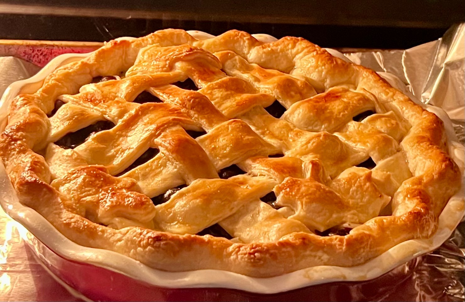 Golden-brown homemade fruit pie with a flaky lattice crust baking in the oven.