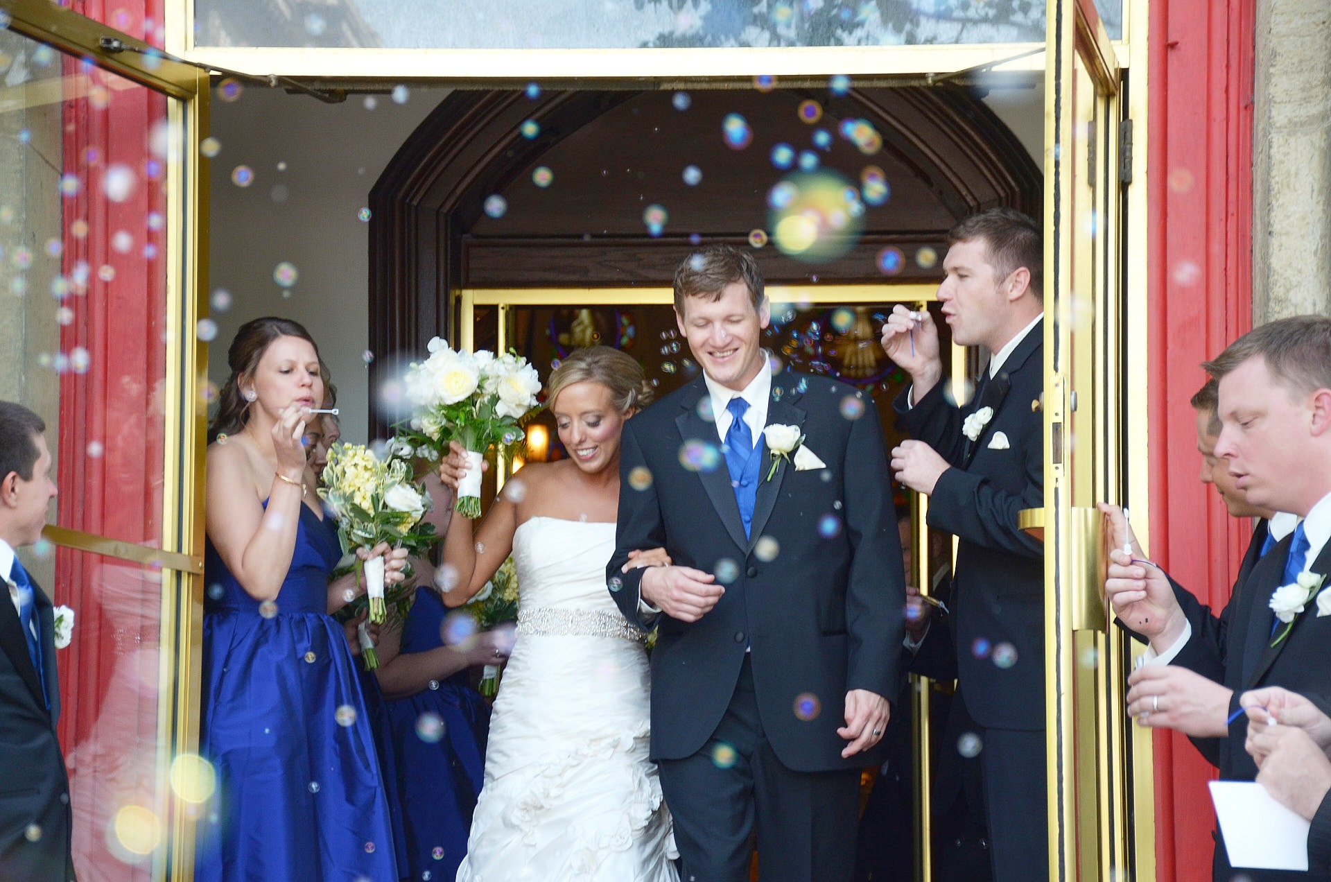 a bride and a groom are walking out of the church door with bubbles generated by guests