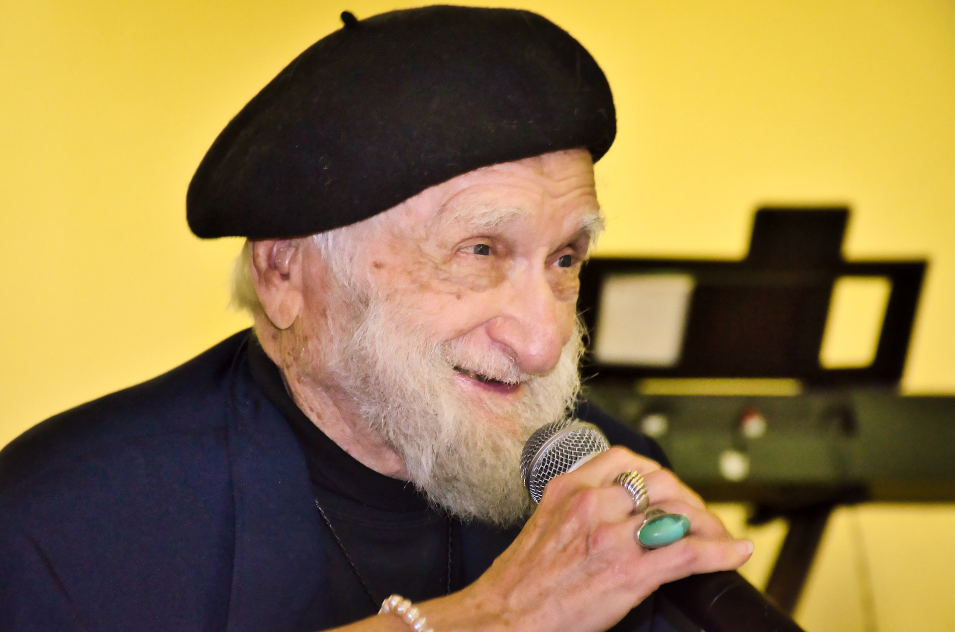 a man with a hat speaking to audiences with a microphone