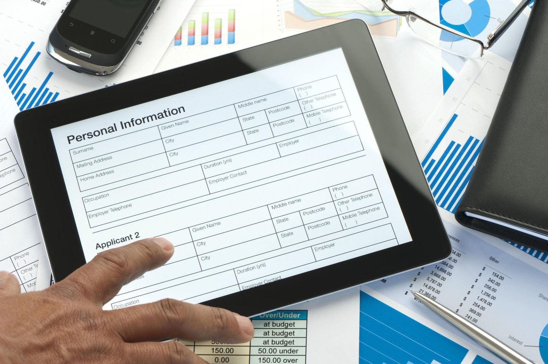 A tablet displaying a form labeled "Personal Information" amidst business documents, charts, and a smartphone.