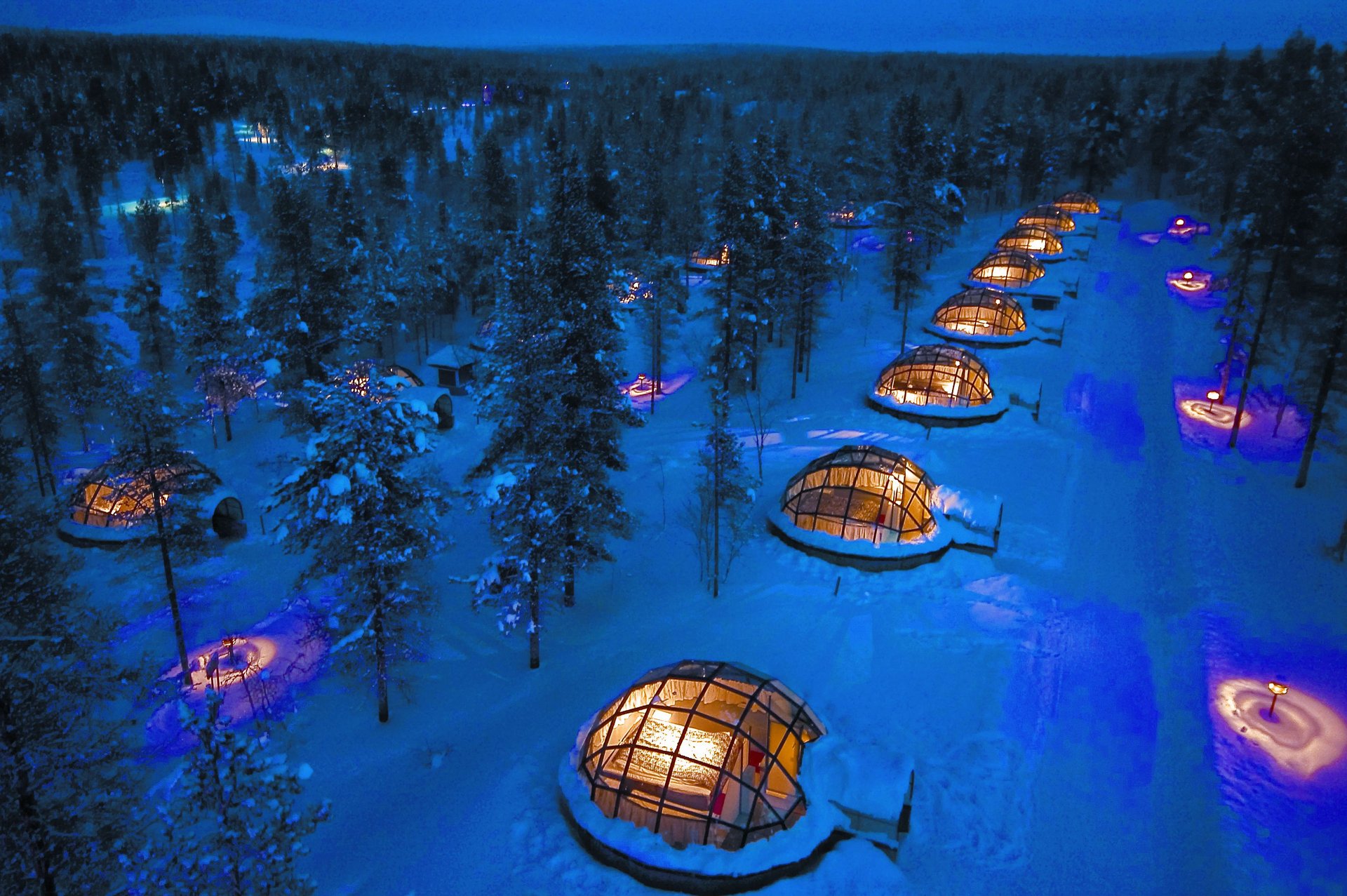 Glowing glass igloos in a snowy Finnish forest at night, perfect for viewing the northern lights.