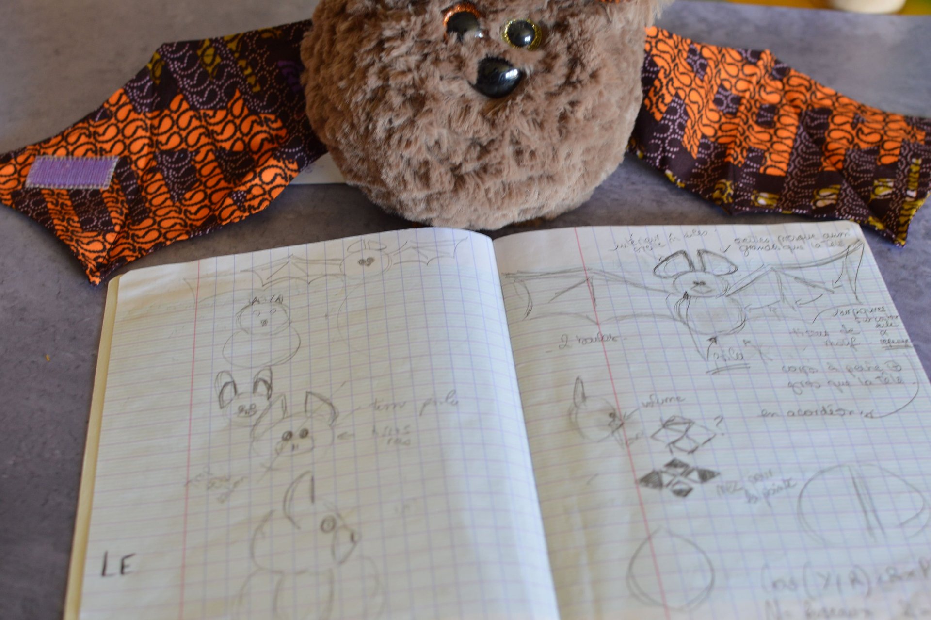 Peluche chauve-souris artisanale posée sur carnet de croquis de création