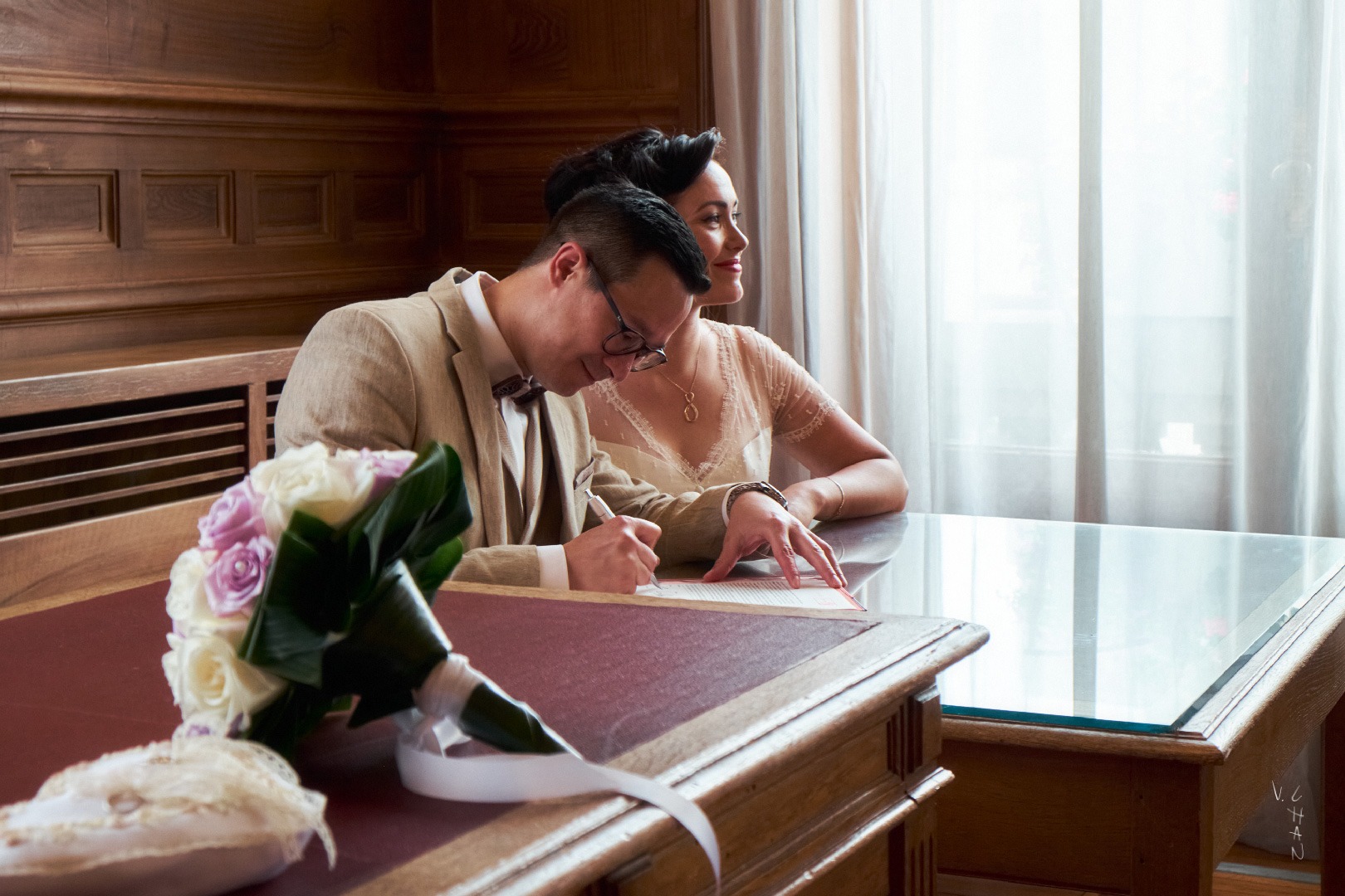 Couple de mariés signant leur acte de mariage et un bouquet de fleurs au premier plan.