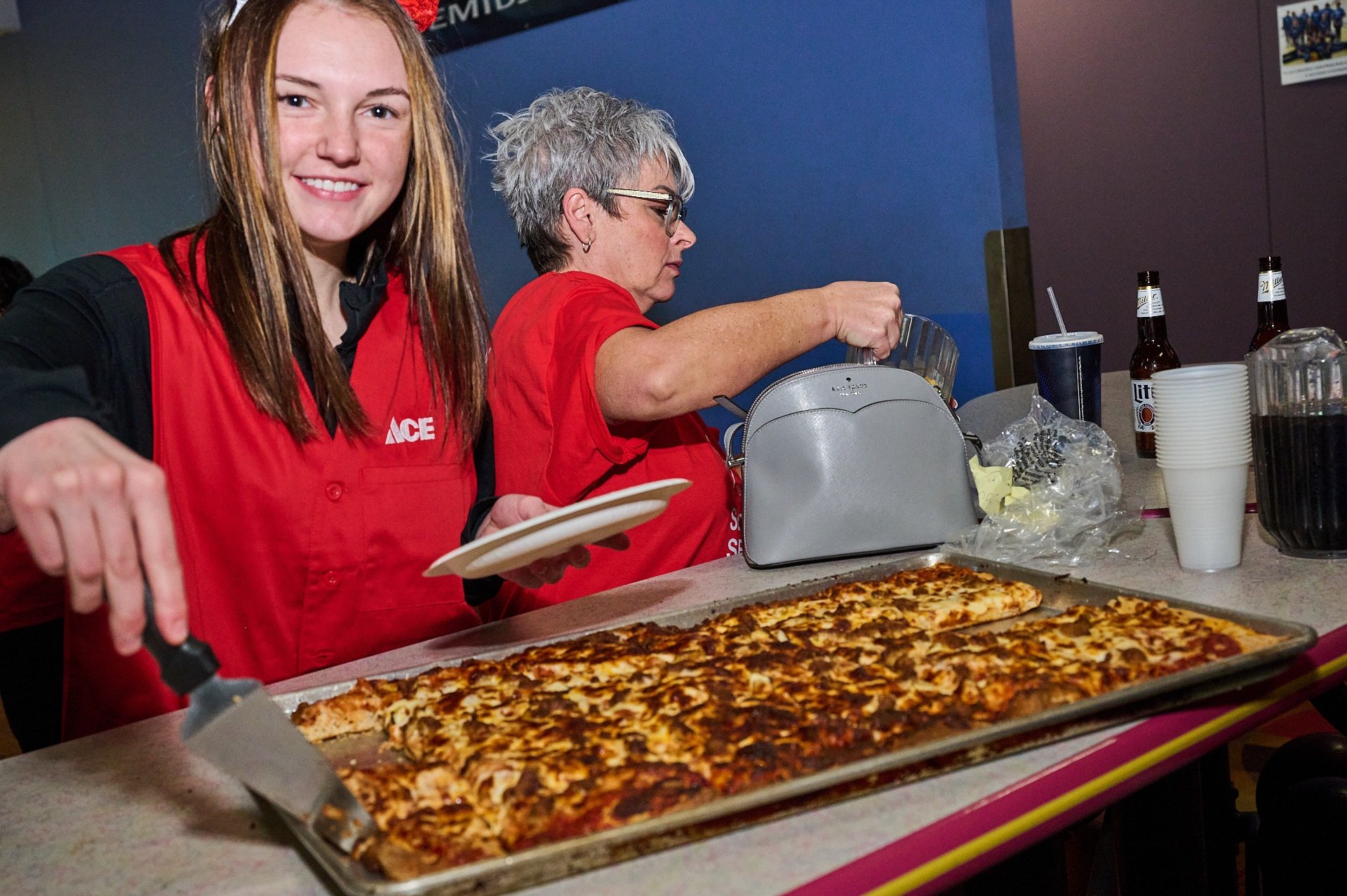 a girl in a red vest is cutting a pizza
