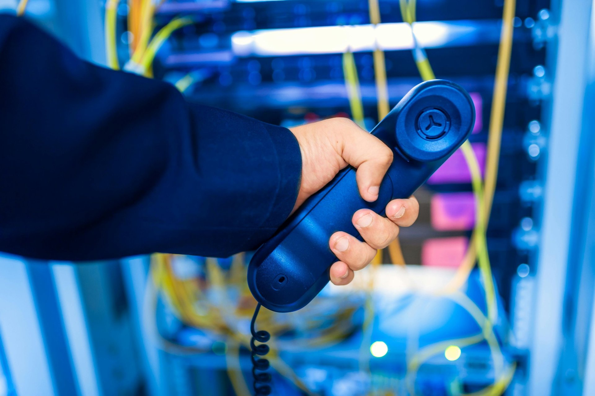 Person holding a phone behind a network rack, representing IT support and remote troubleshooting services