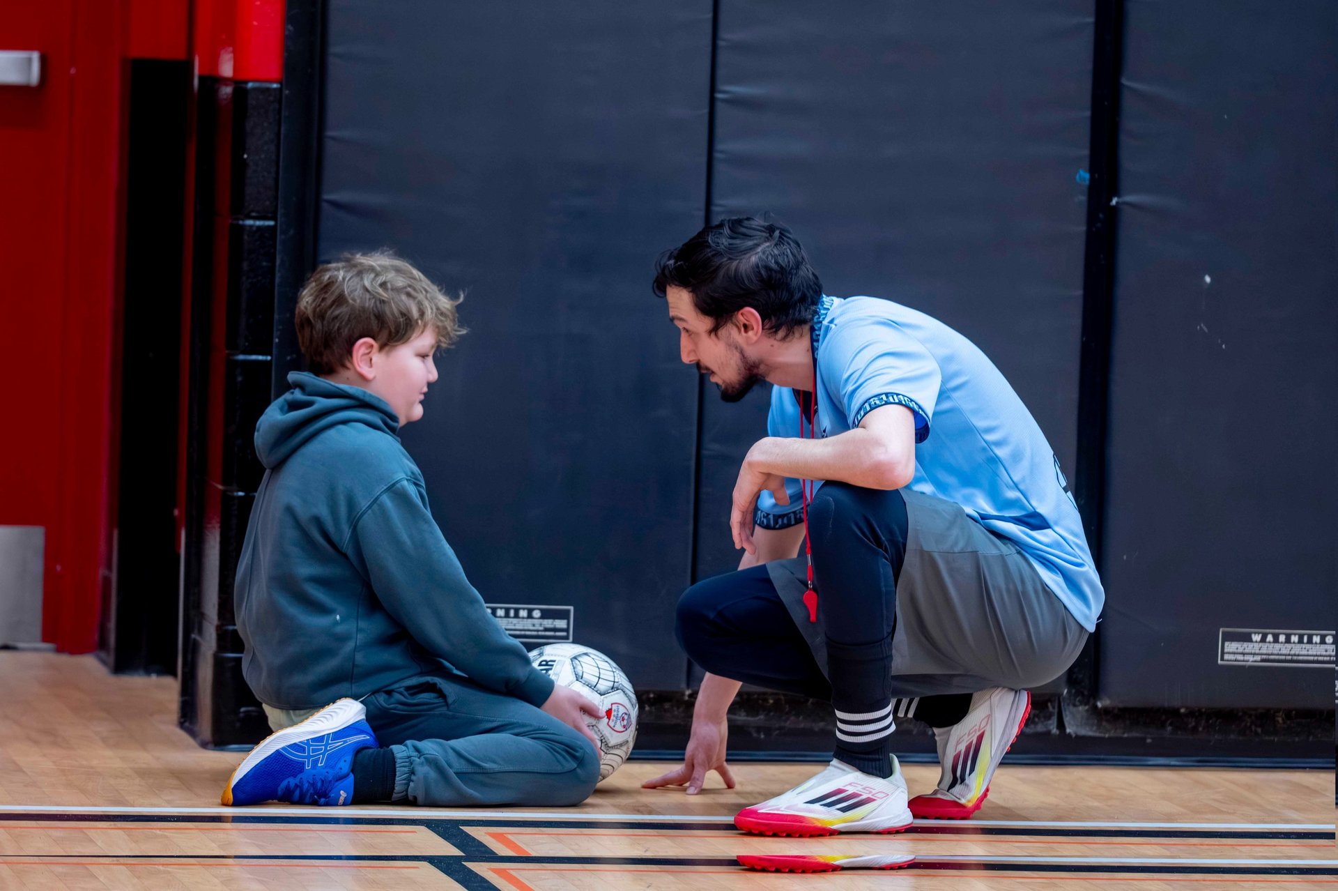 A soccer coach talking to a young boy at a soccer MVB FC class in Mississauga