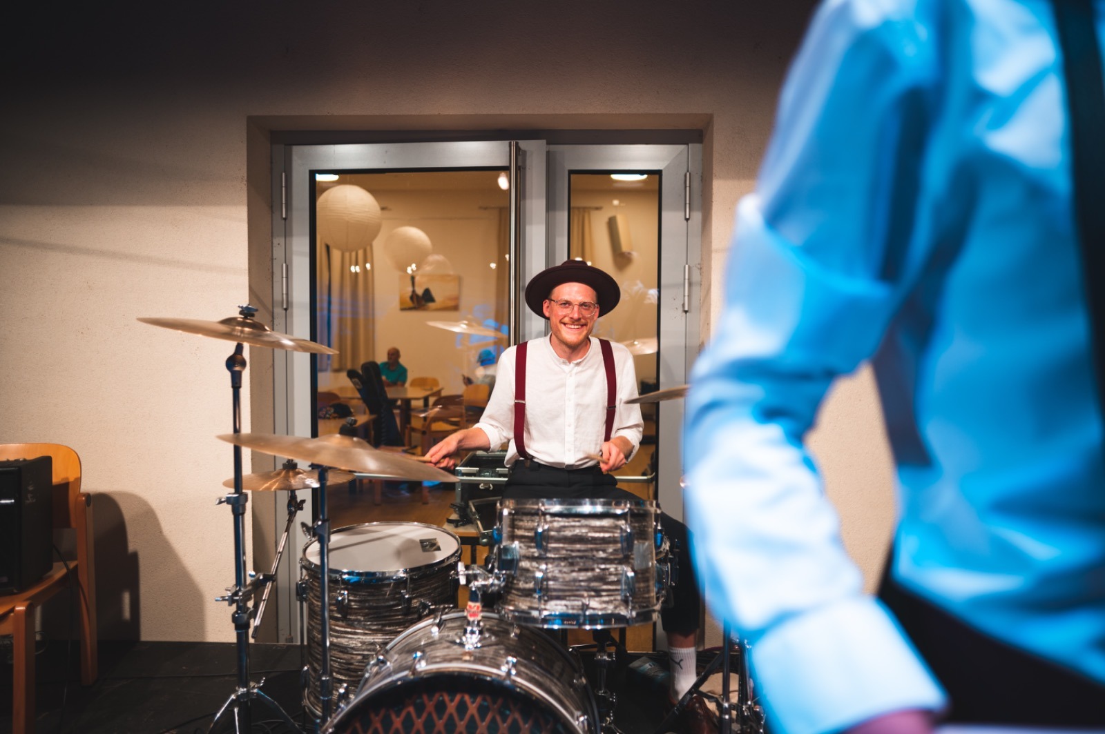a man in a hat and suspenders playing drums