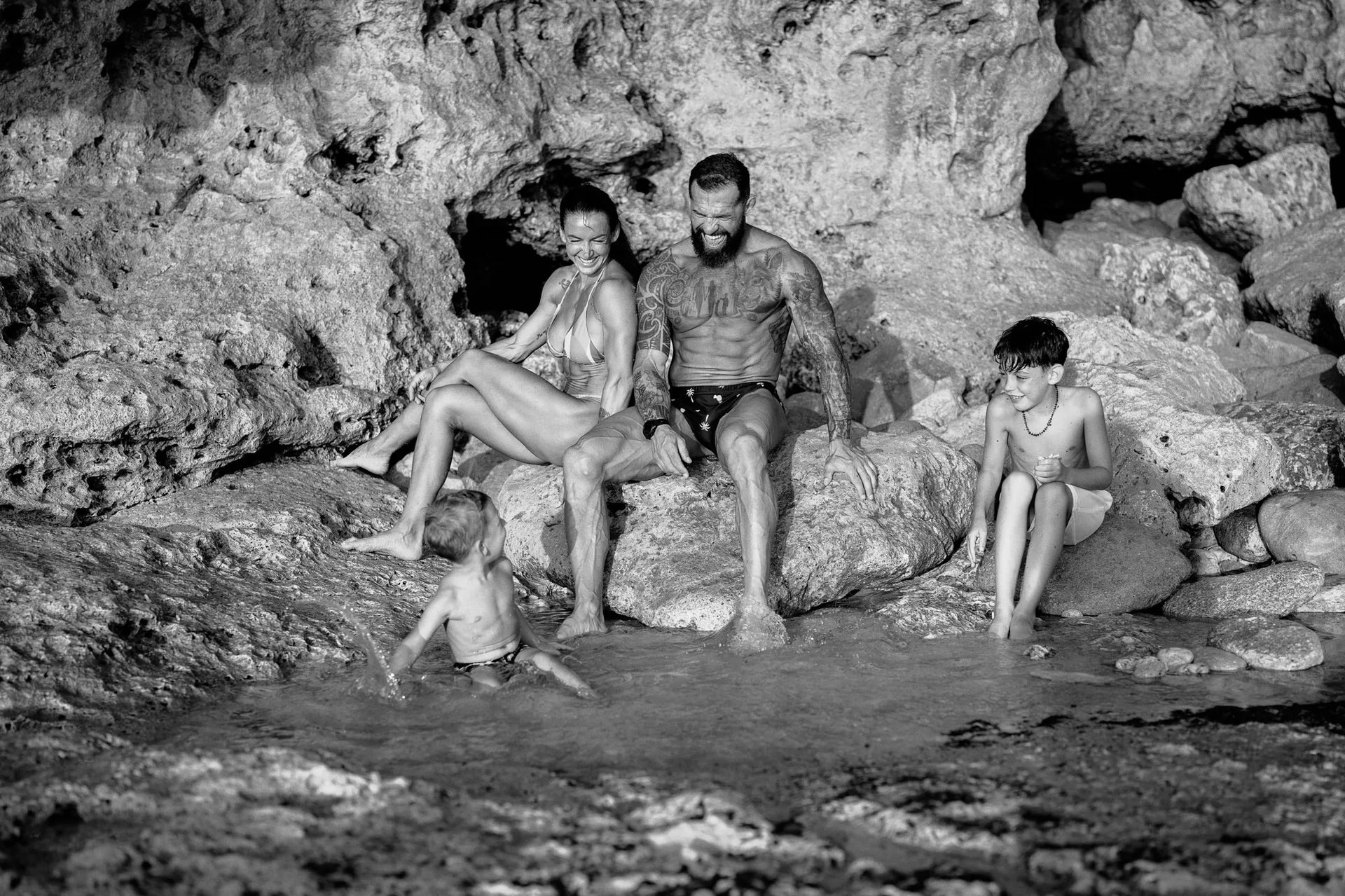 Family sitting together on coastal rocks during a candid family photography session at Dreamland Beach Bali.