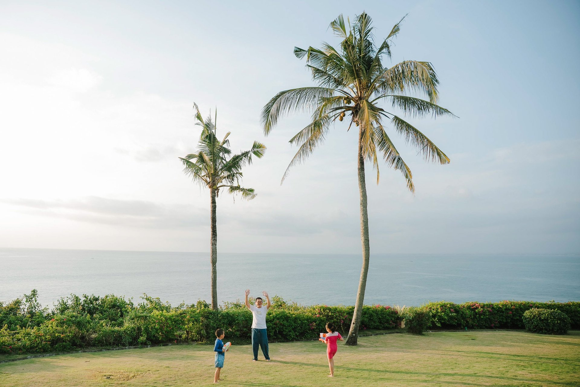 Playful sibling moment on tropical garden lawn at AYANA Villas Bali, natural family lifestyle photography