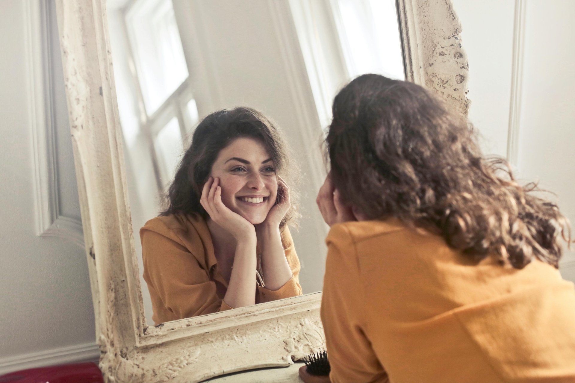 a woman in a yellow shirt is smiling and looking at her reflection in the mirror