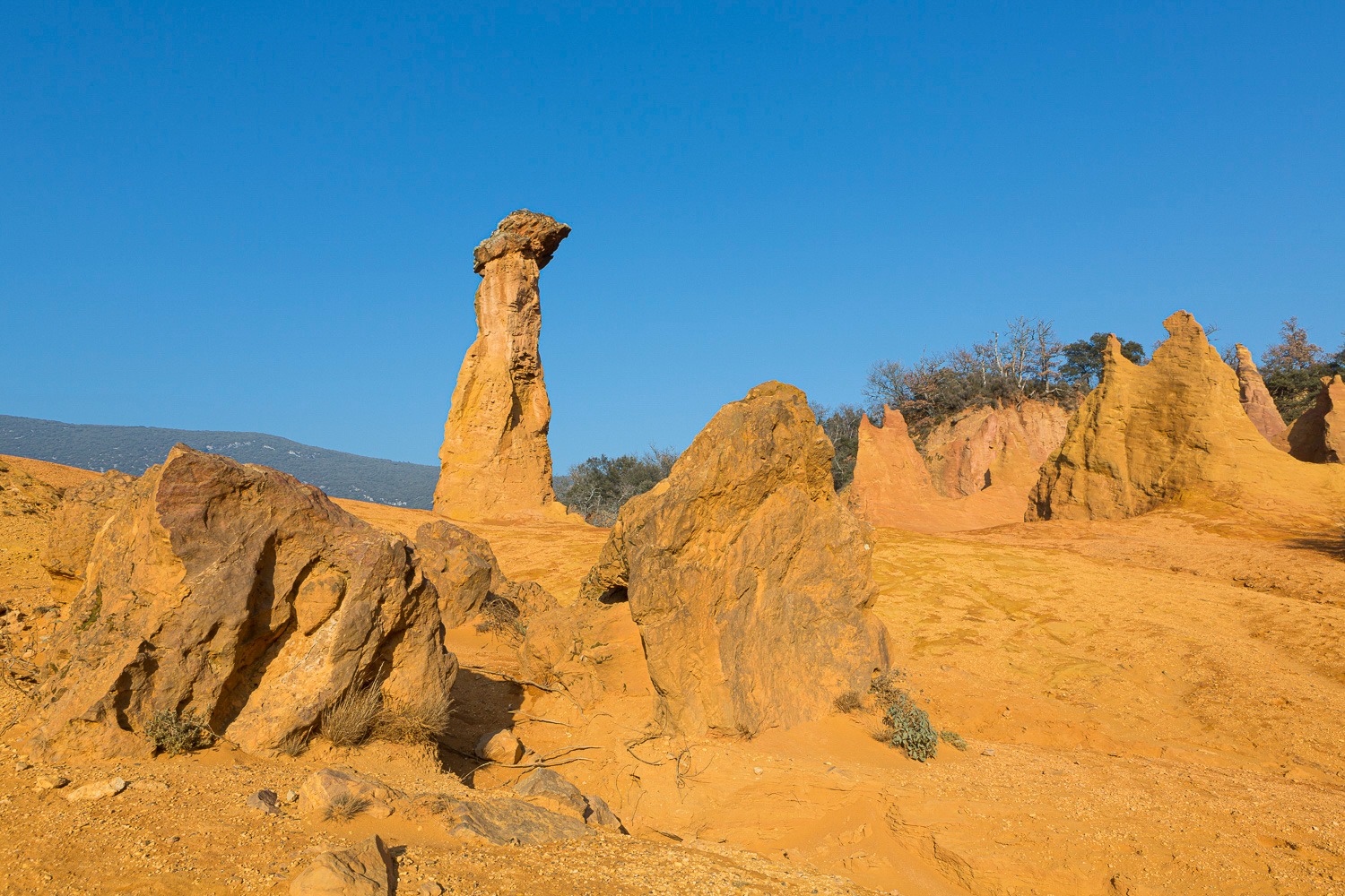 Tall orange ochre rock formation at Colorado Provençal in Rustrel, France, under a clear blue sky.