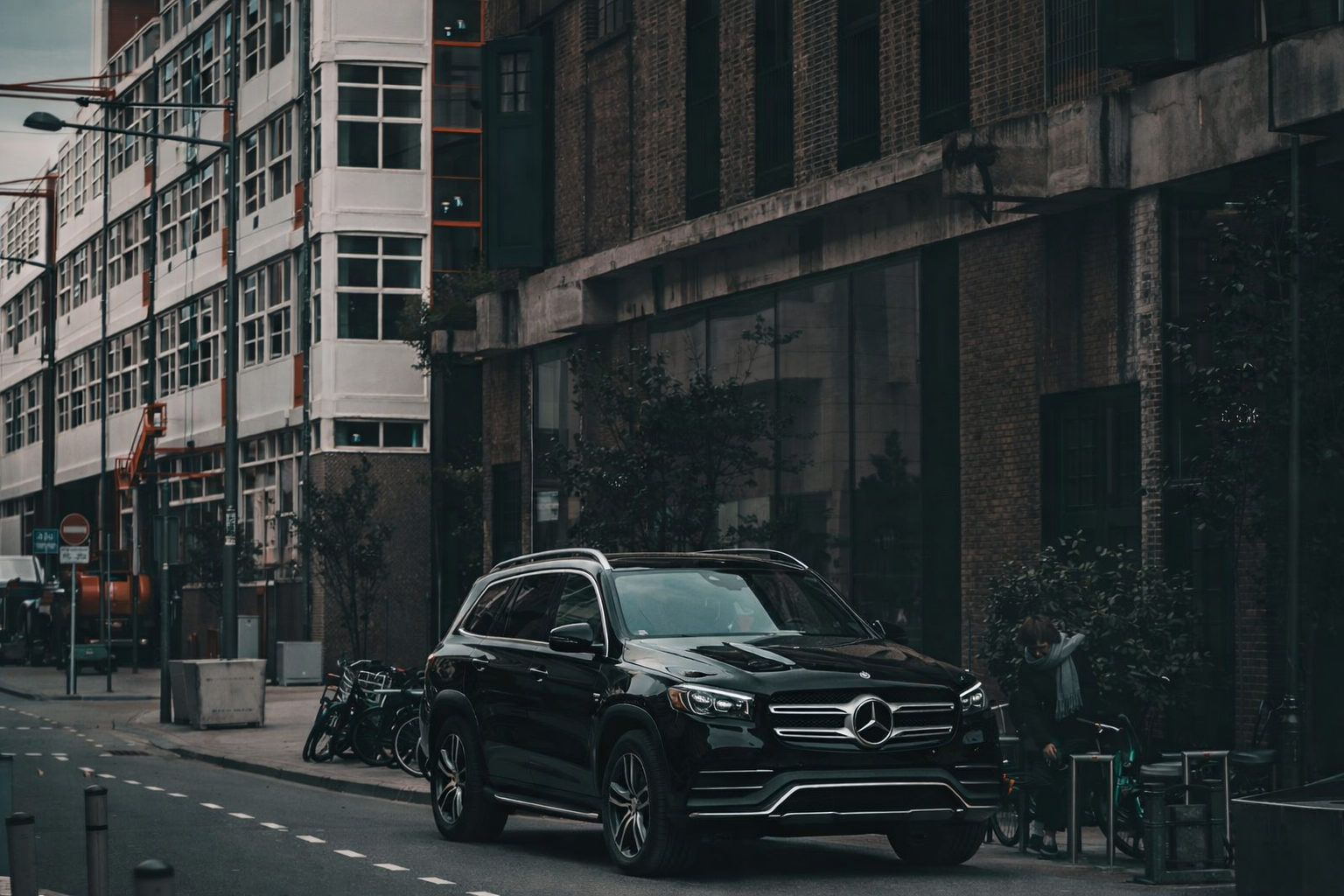 A black Mercedes-Benz SUV parked on a city street in front of industrial brick buildings.