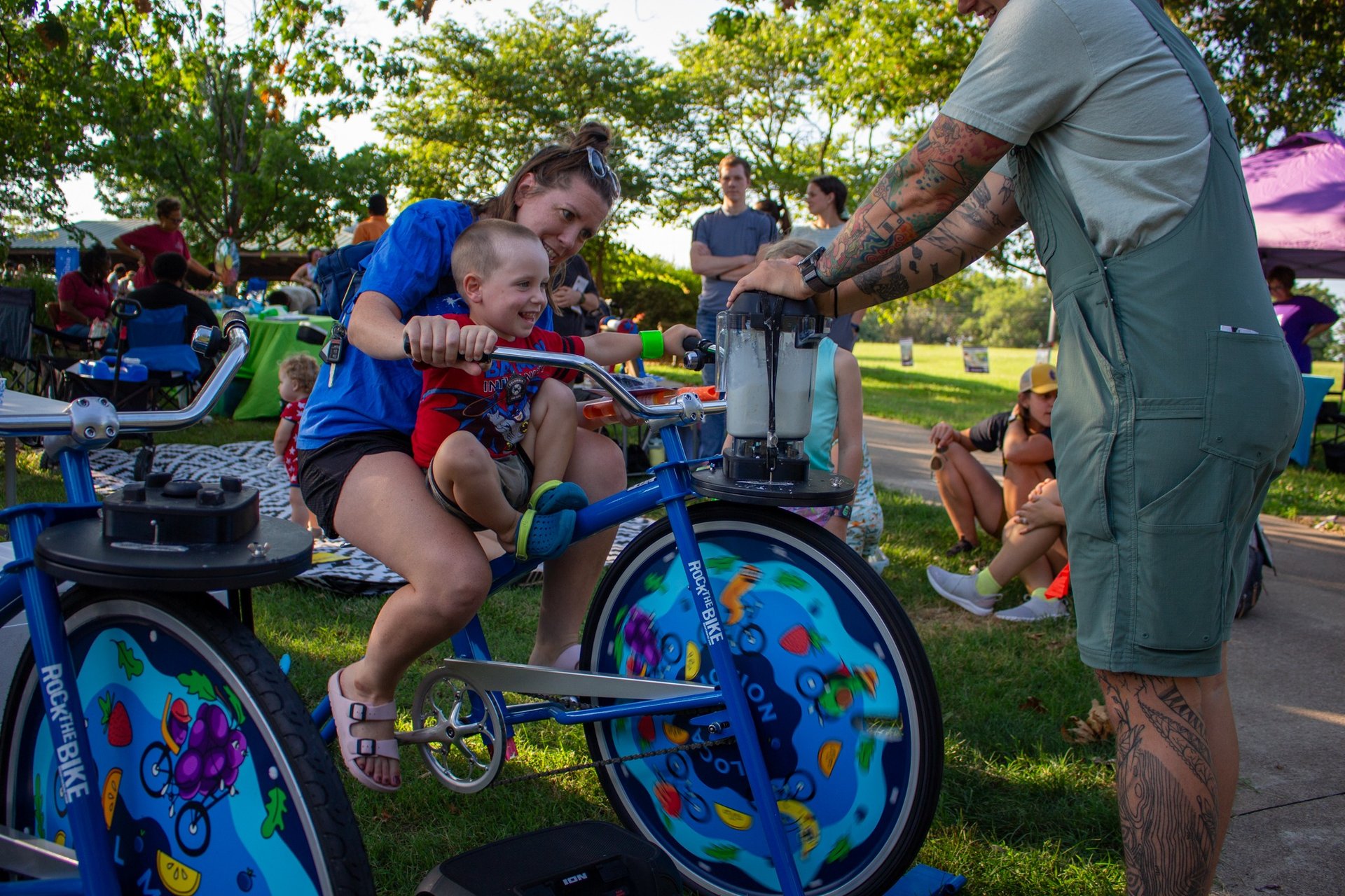 A little kid and a parent powering a smoothie on our blender bike