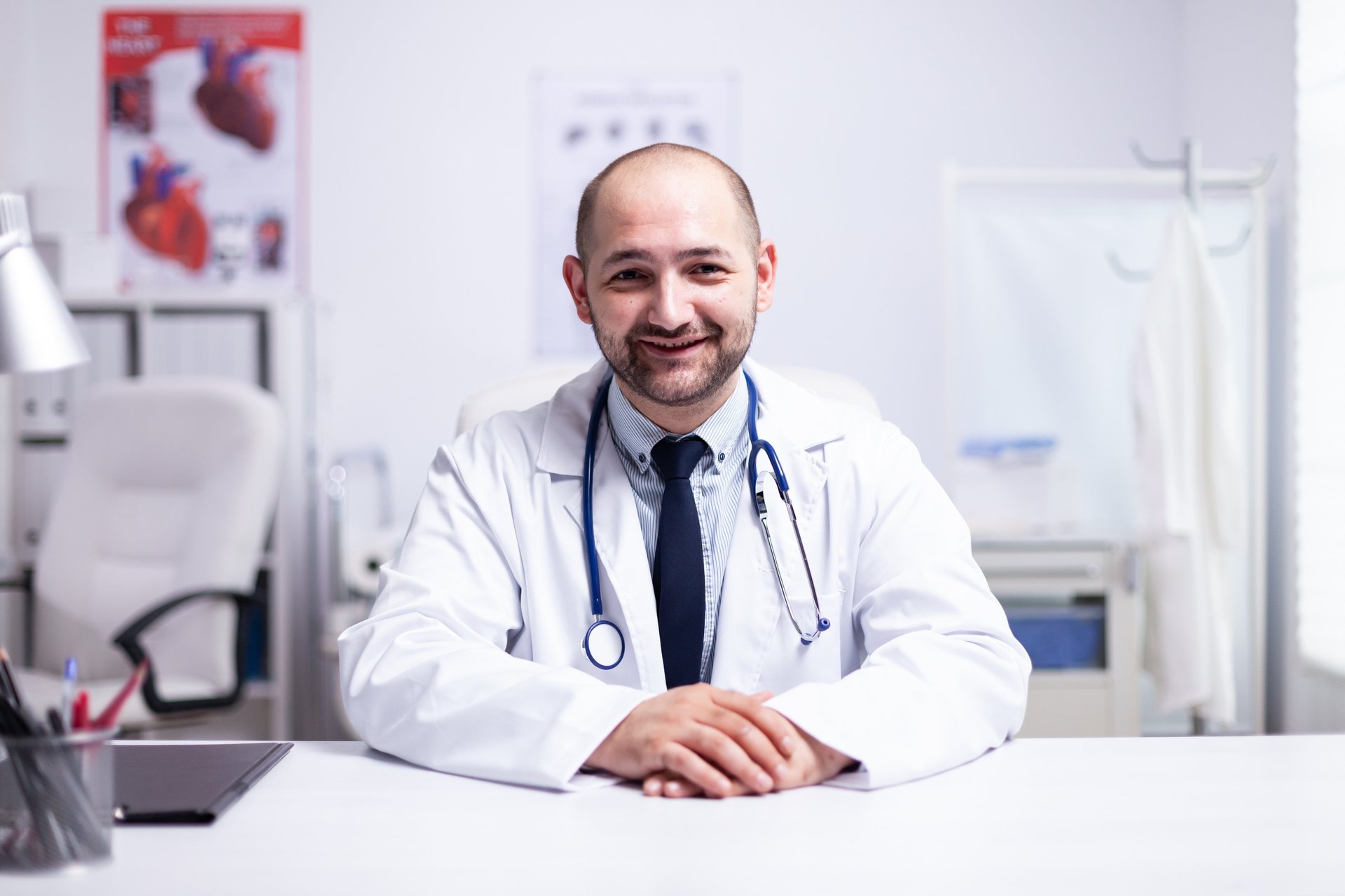 profissional da área da saúde sentado em consultório médico com jaleco e estetoscópio