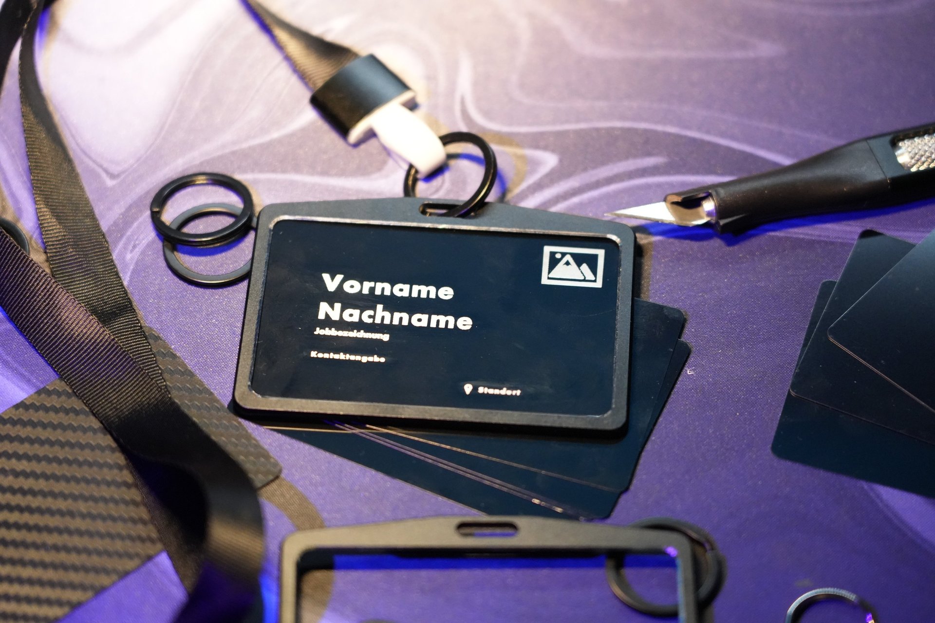 Customized black business ID card in a holder with a neck lanyard on a purple surface.
