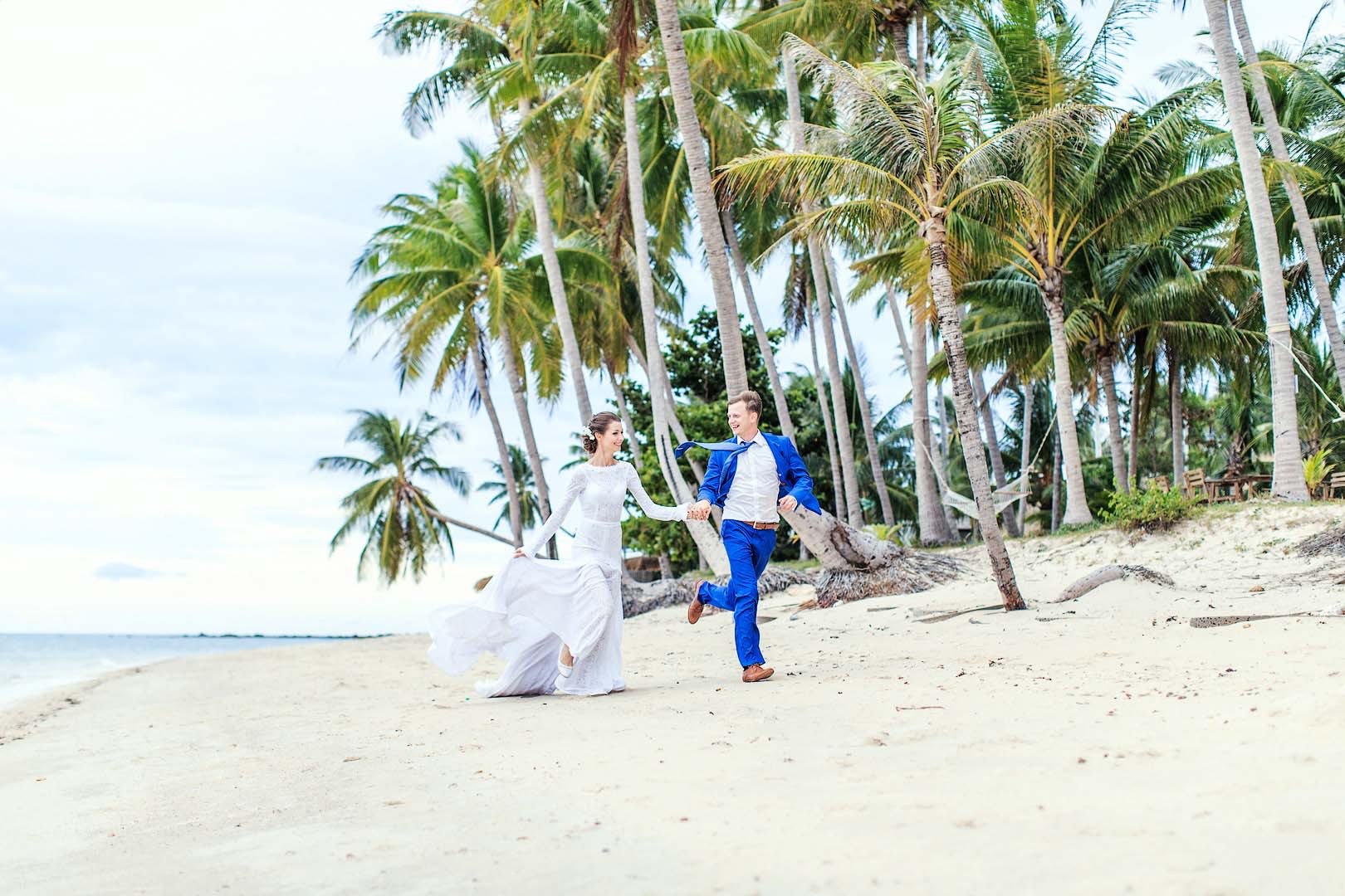 Wedding couple running on Ong Lang Beach under palms