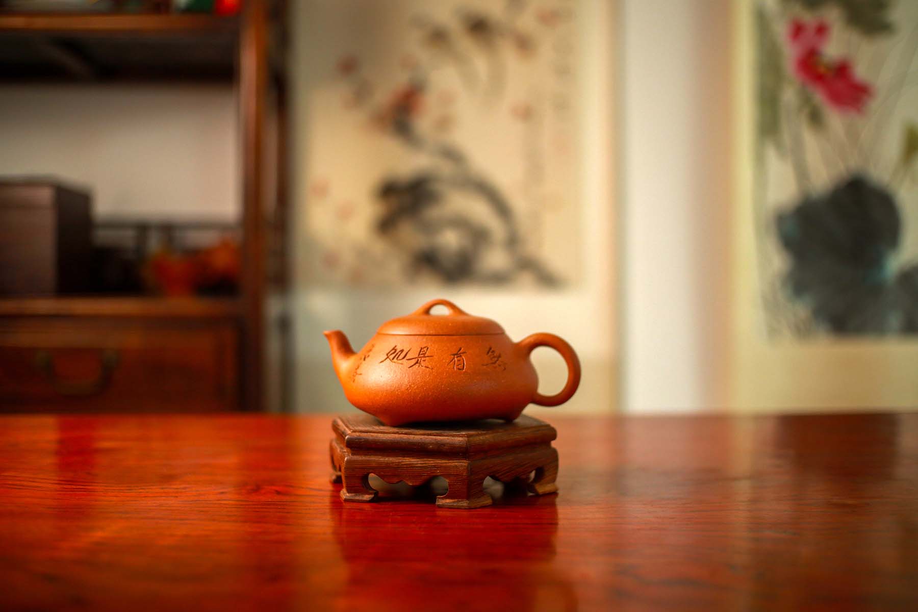 A yellow Yixing teapot engraved with Chinese characters is placed on a wooden stand