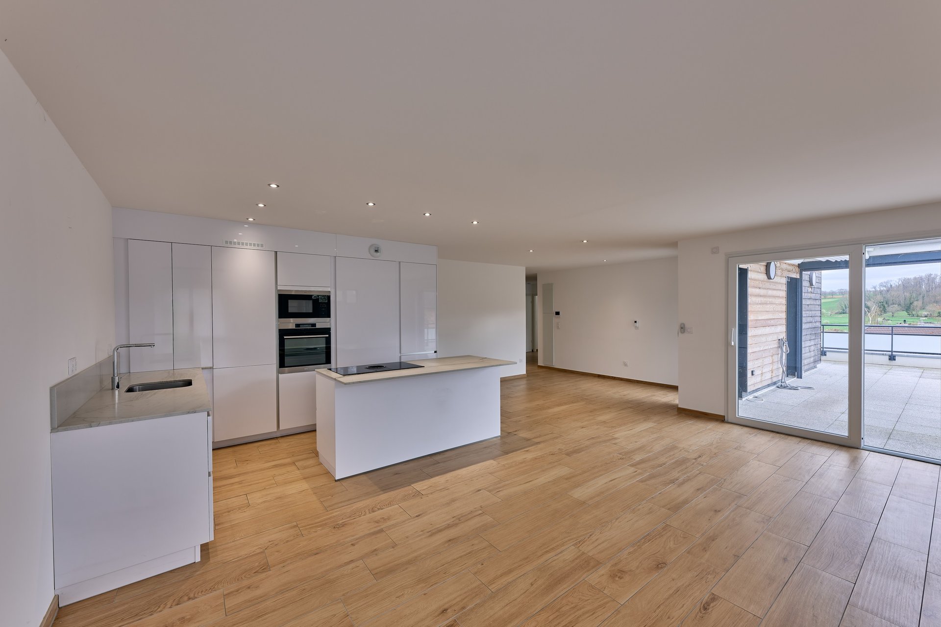 Cuisine moderne minimaliste blanche avec îlot central, parquet et grandes portes-fenêtres