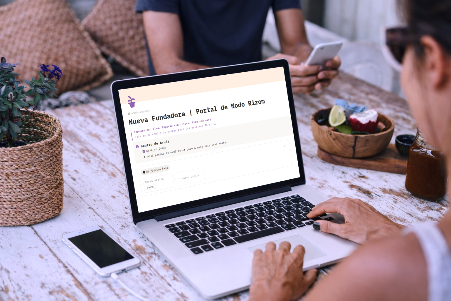 Woman working on a laptop displaying the Nodo Rizom website portal while sitting at an outdoor table.