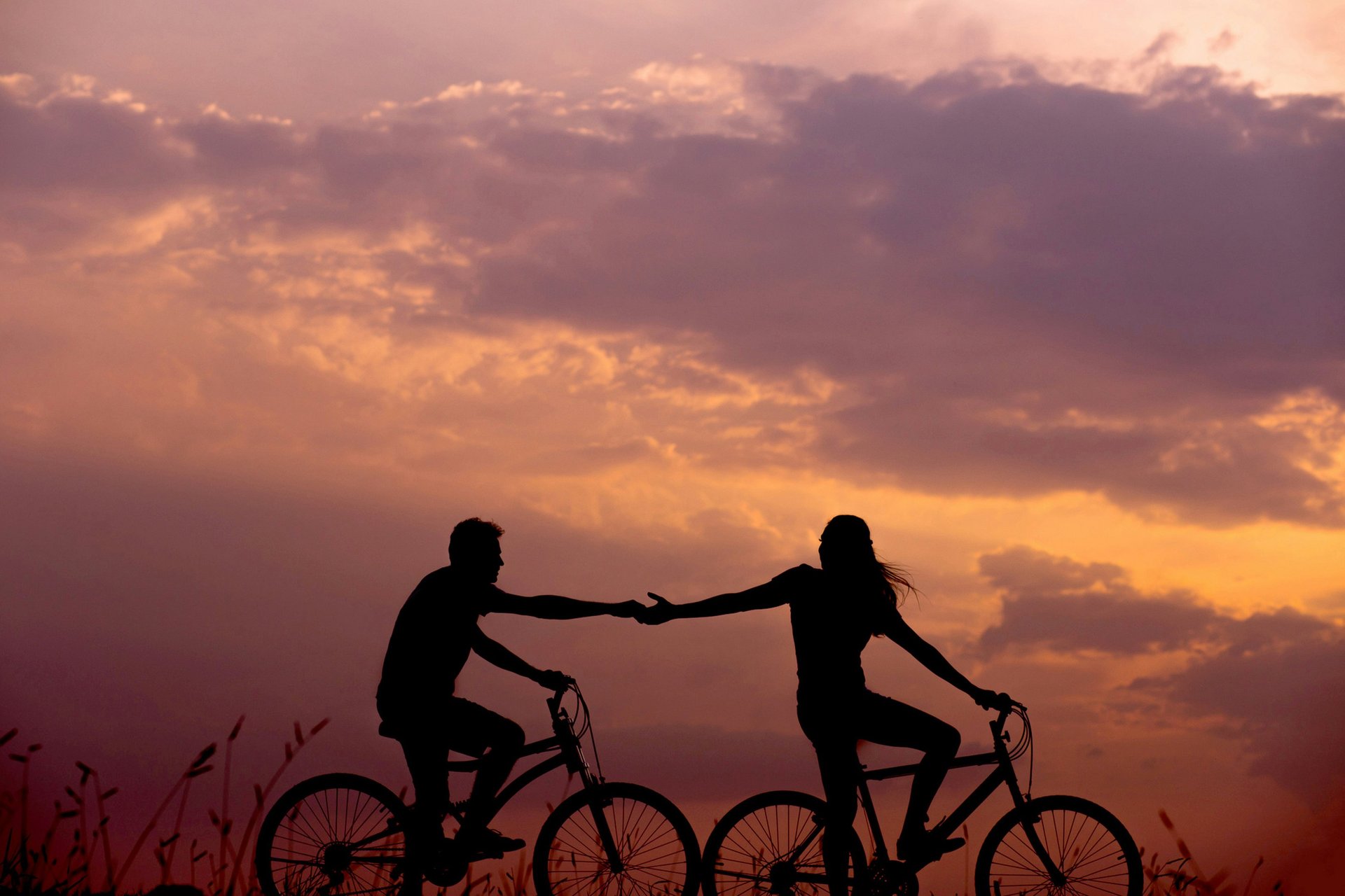 A woman reaching for her man while riding a bicycle and trying to reconnect with her man while biking through the countryside