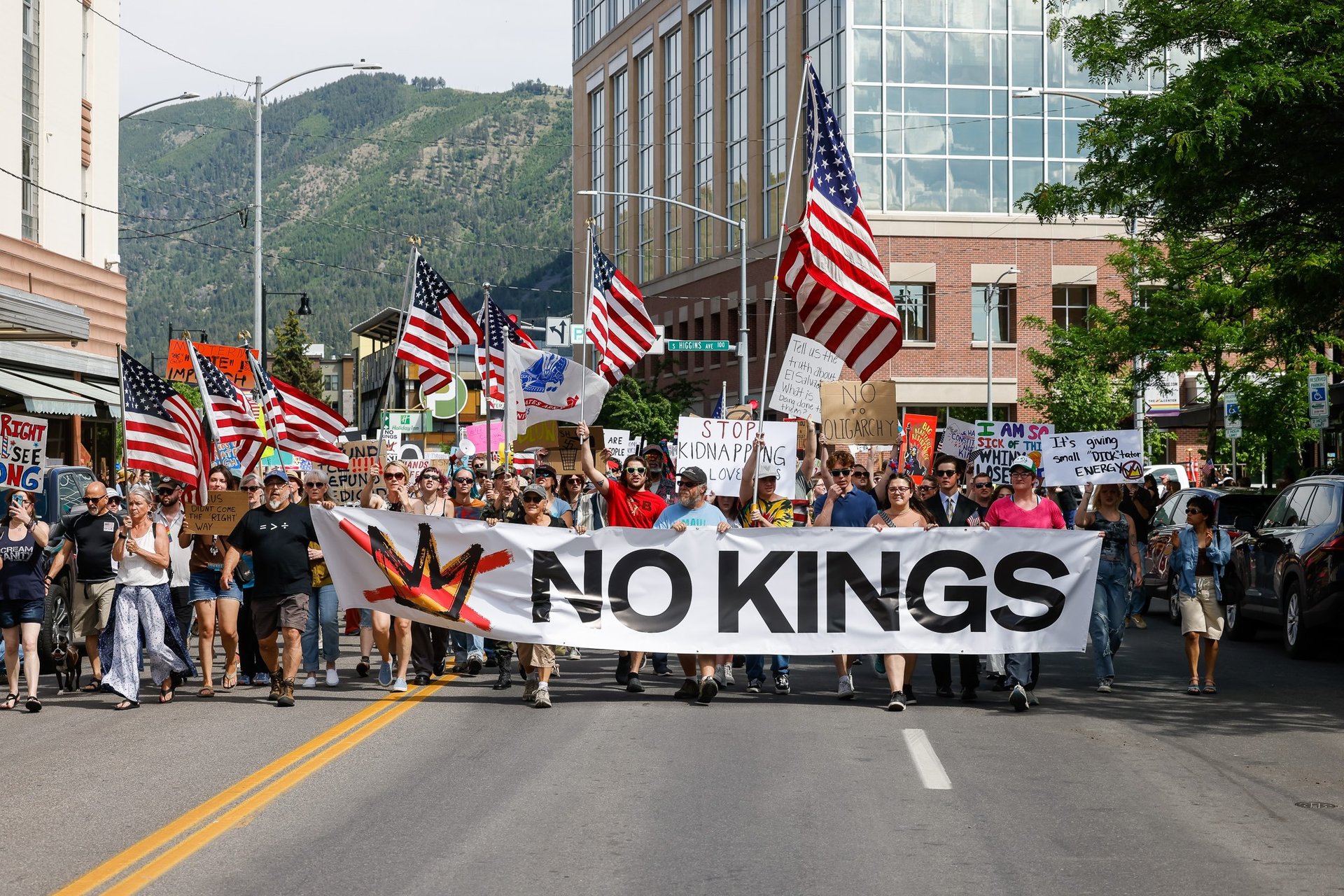 Protesters march down a city street holding American flags and a large No Kings banner during a political demonstration.