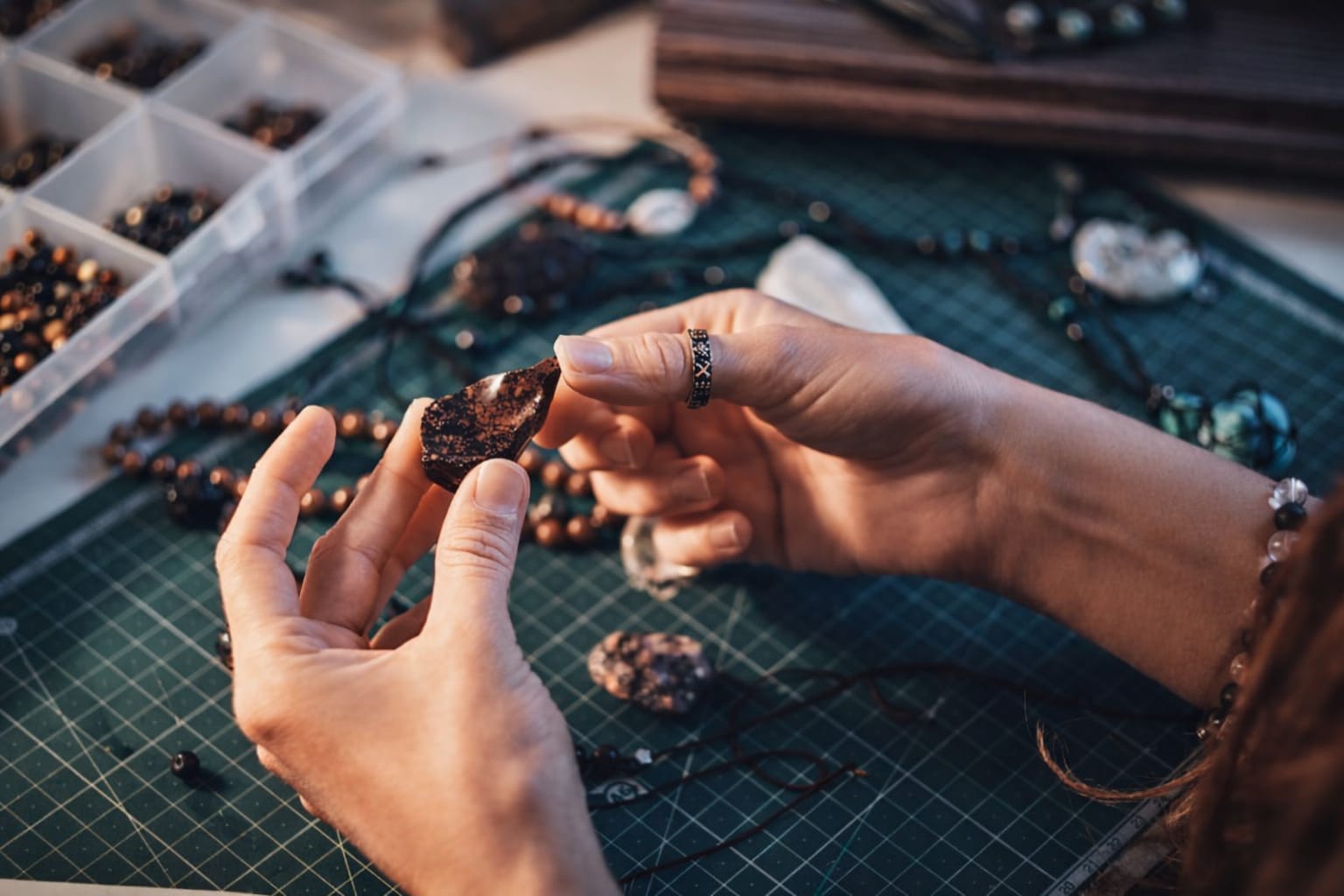 Manos de artesana sosteniendo piedra natural oscura sobre mesa de corte verde con herramientas y cue
