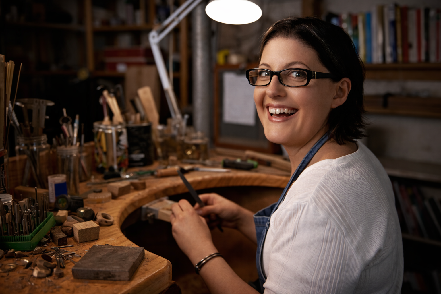 Artesana joyera sonriendo mientras trabaja en su mesa de trabajo con herramientas de joyería