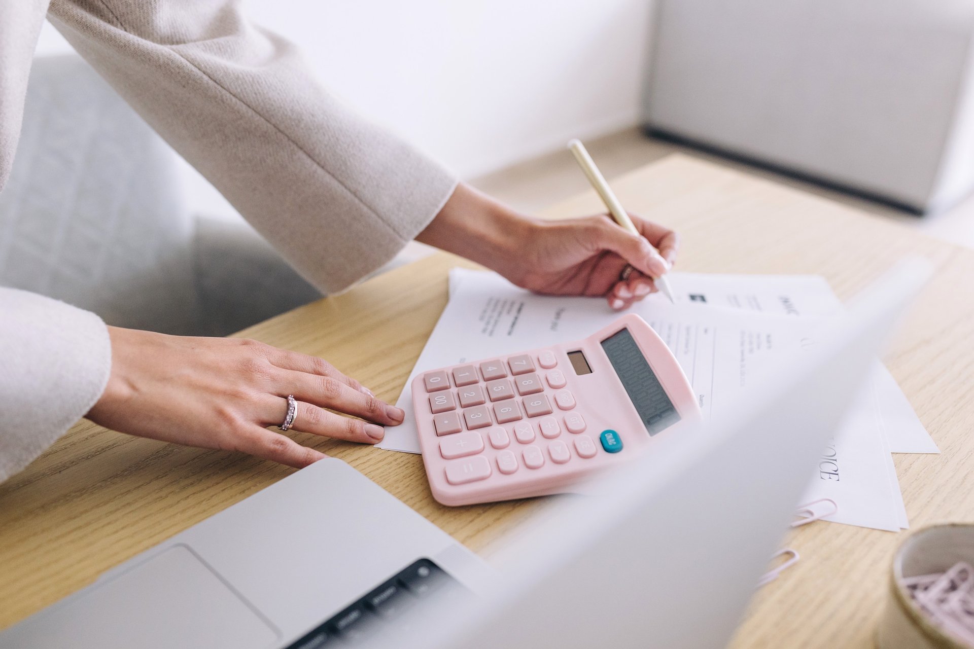 Businesswoman using a pink calculator and pen to calculate business finances and invoices at a desk.