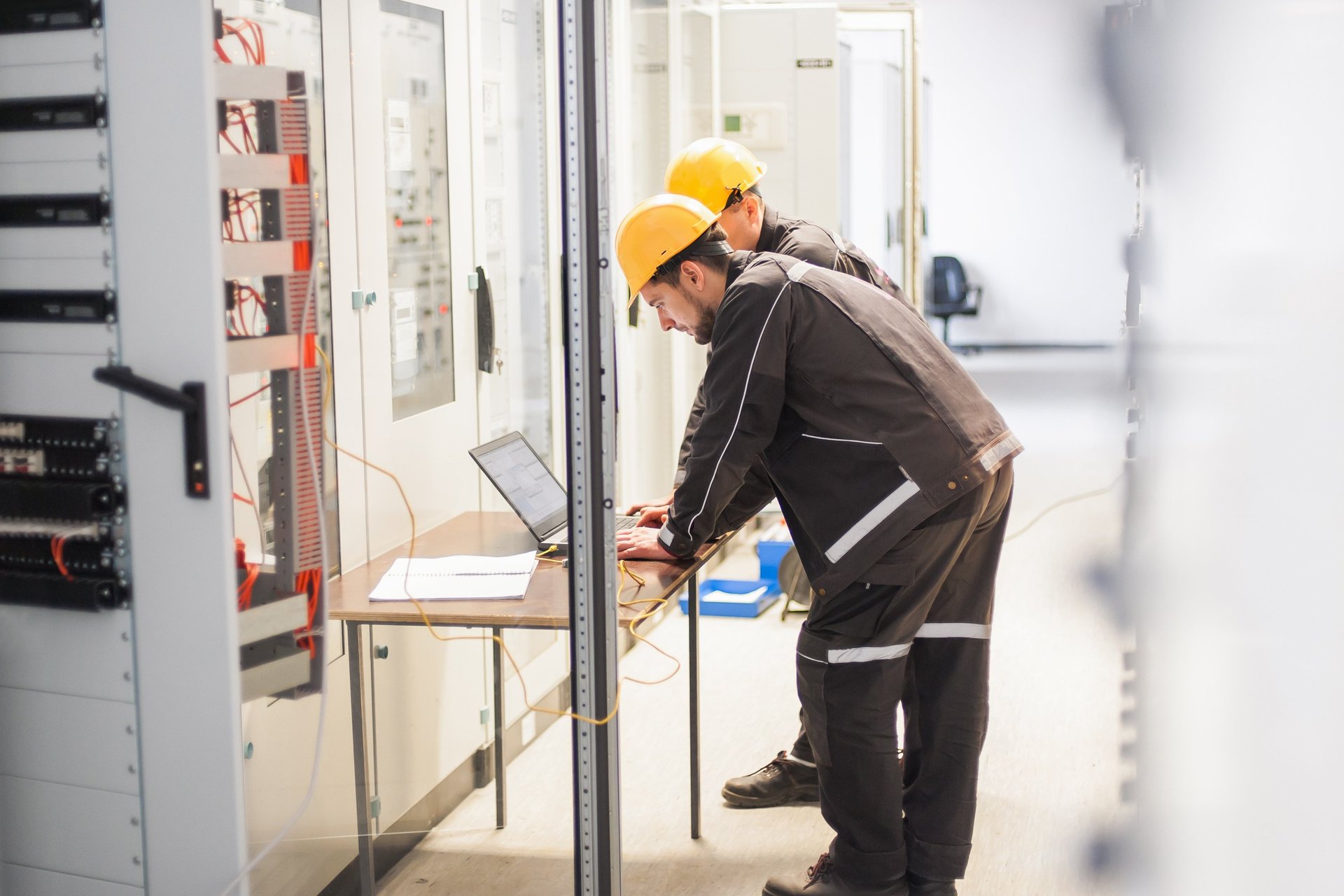 Technicians in hard hats using a laptop for electrical maintenance.