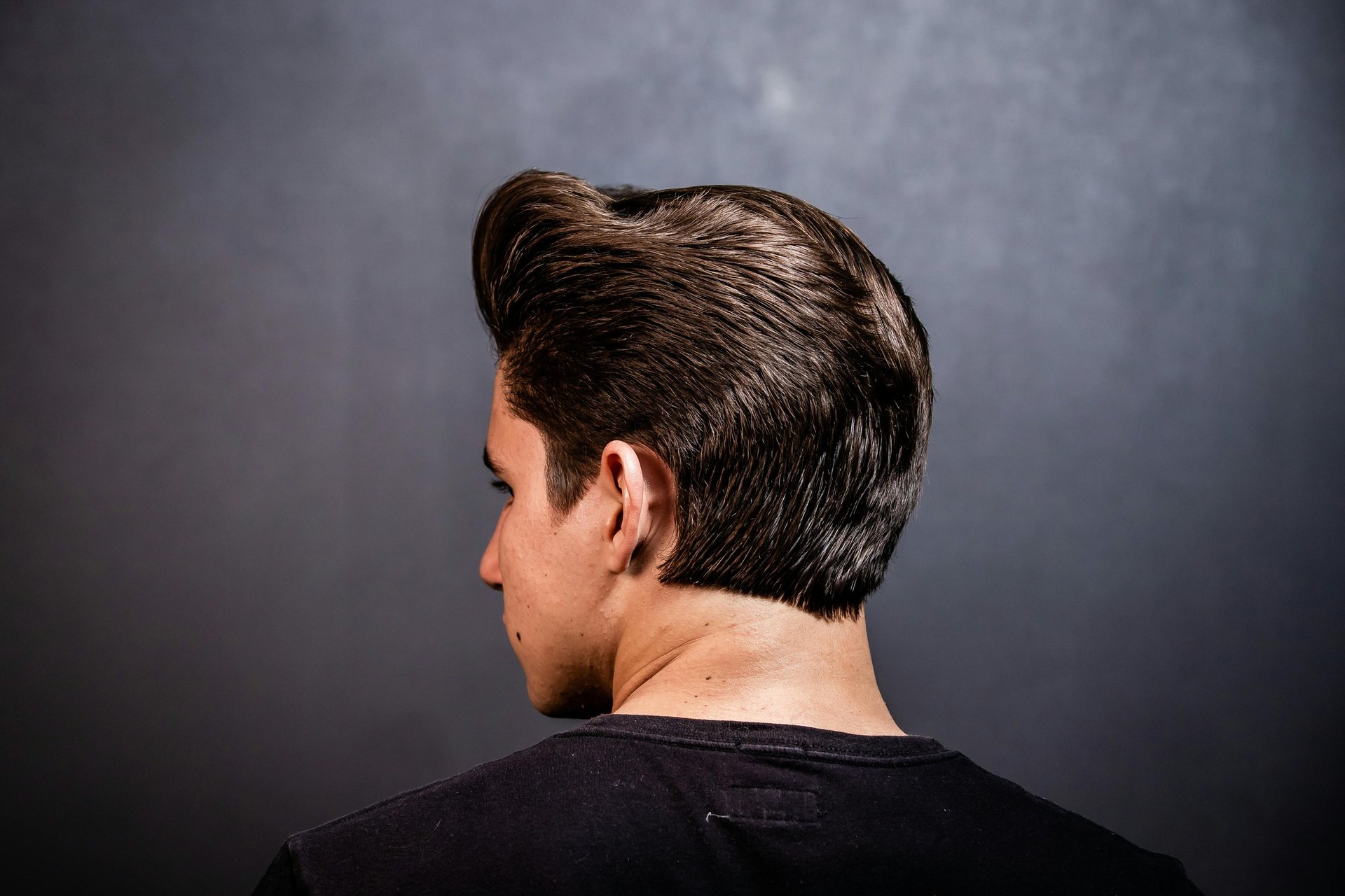 Young man showcasing a shiny, classic rockabilly pompadour hairstyle with a clean taper fade.