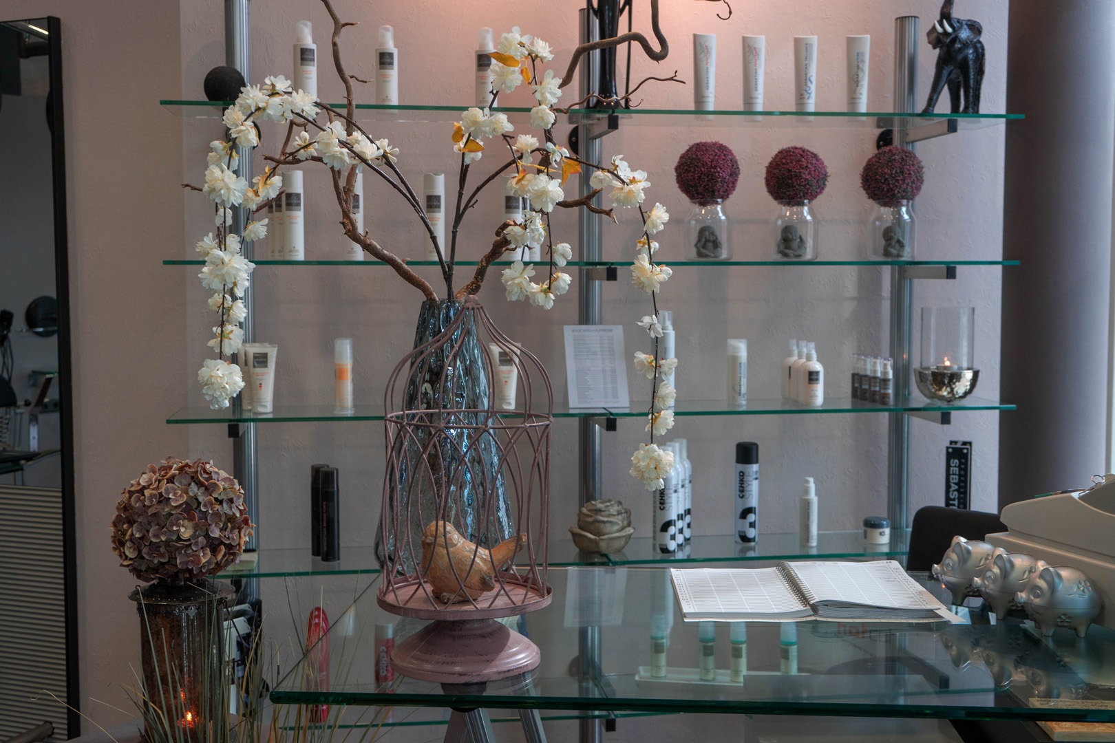 A boutique salon reception desk featuring white flowers in a birdcage vase and professional hair care products.
