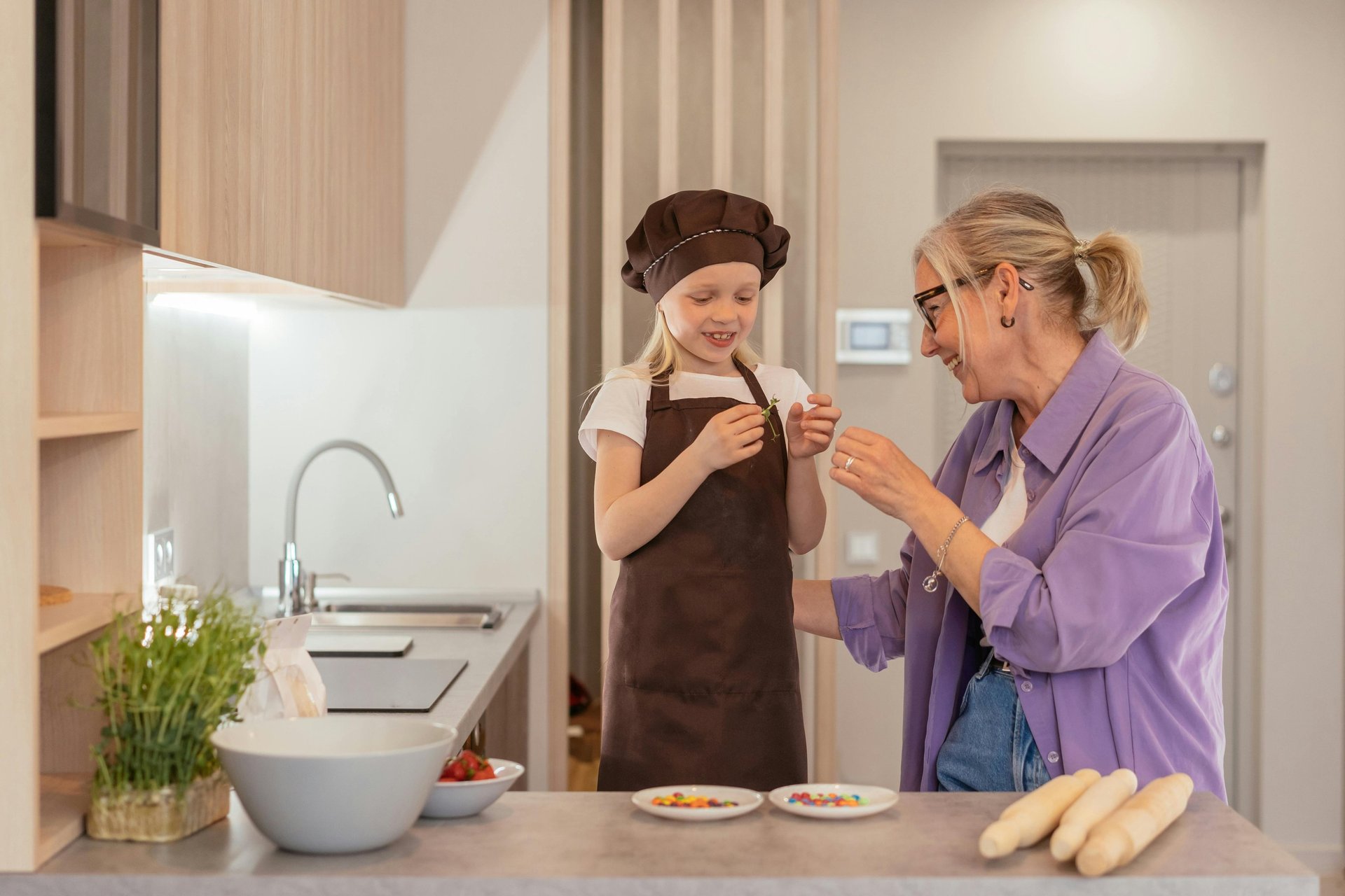 a grandmother standing in her kitchen with a grand daughter preparing food together
