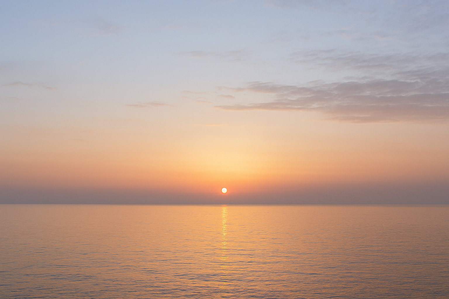 A soft sunrise over a calm sea, the sky shifting from darkness to light 