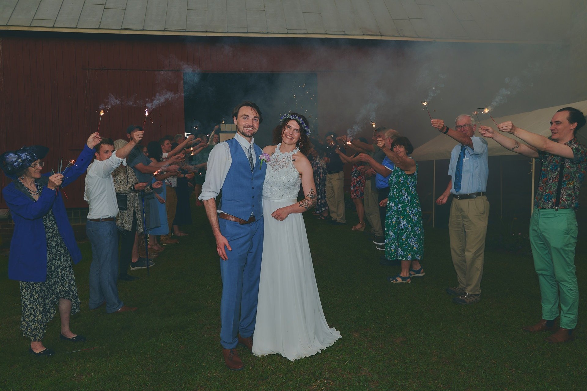 a bride and groom are standing in front of a barn with guests holding up sparklers