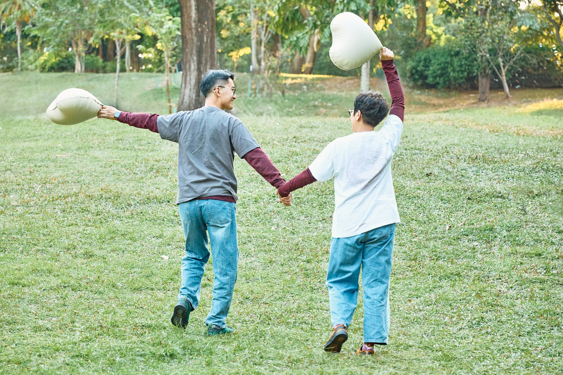 A happy young couple holding hands and carrying heart-shaped balloons in a lush green park.