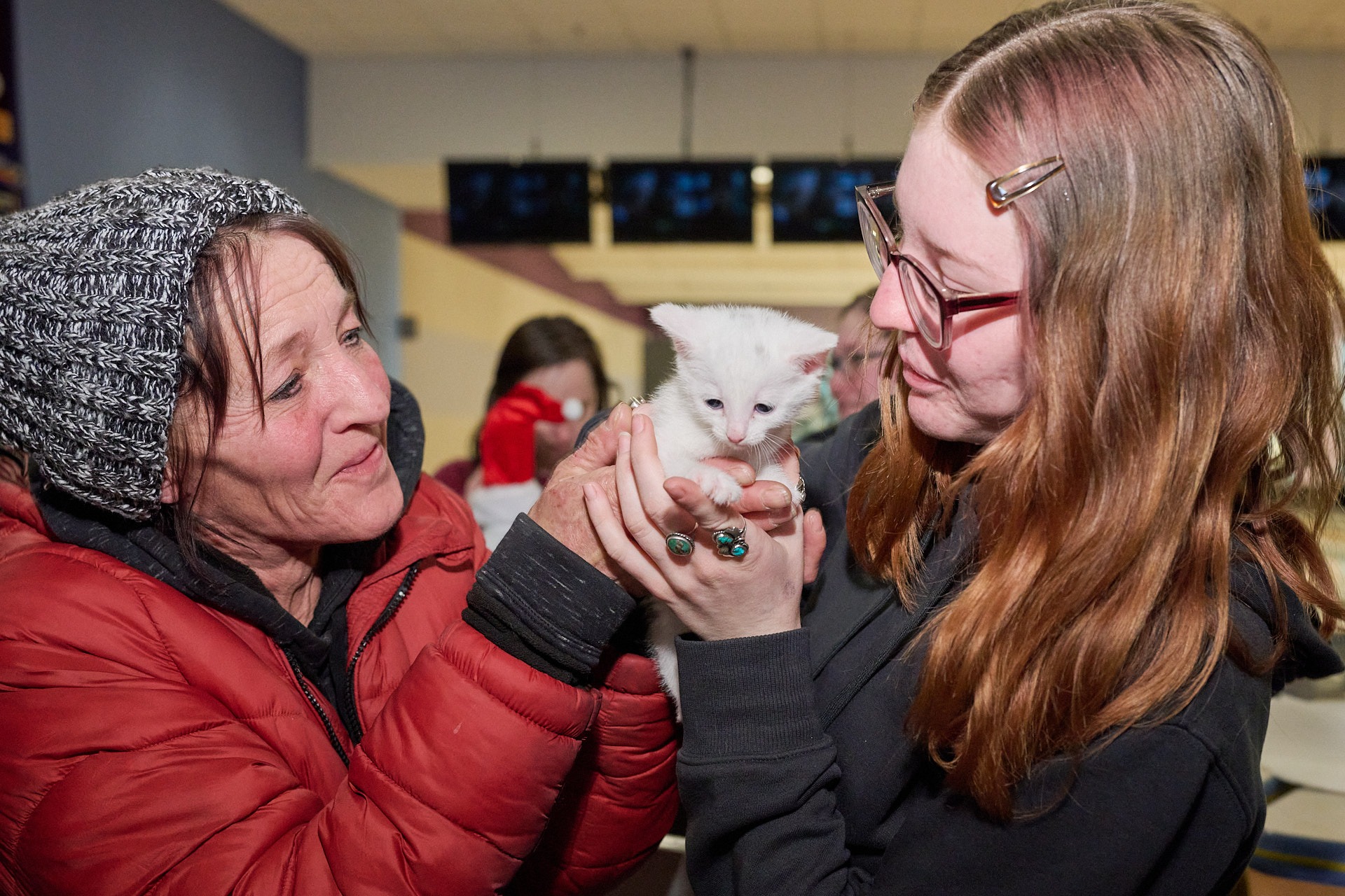 two women holding a white kitten in a room