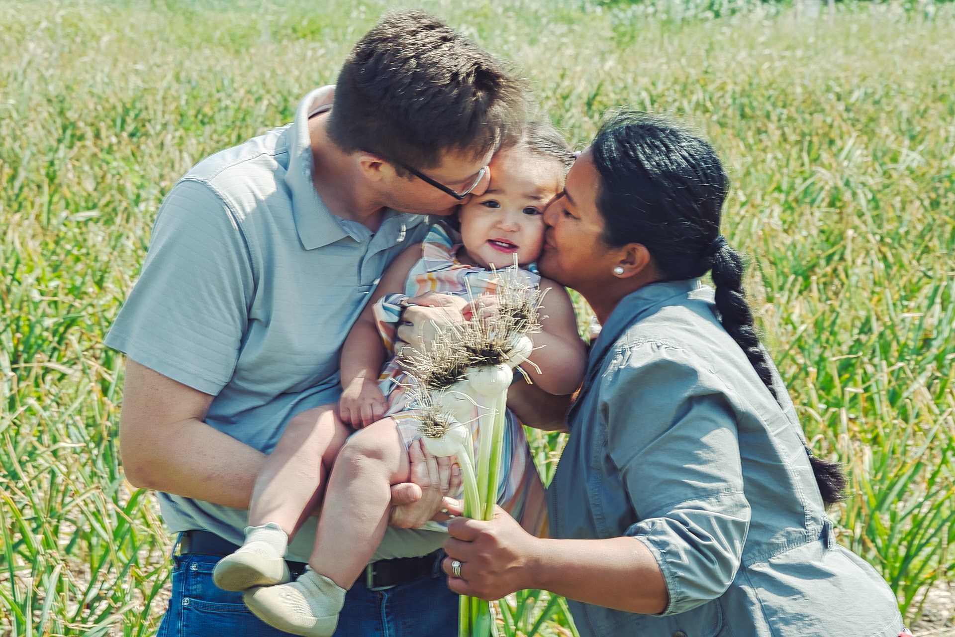 a man and woman holding a baby in a garlic field