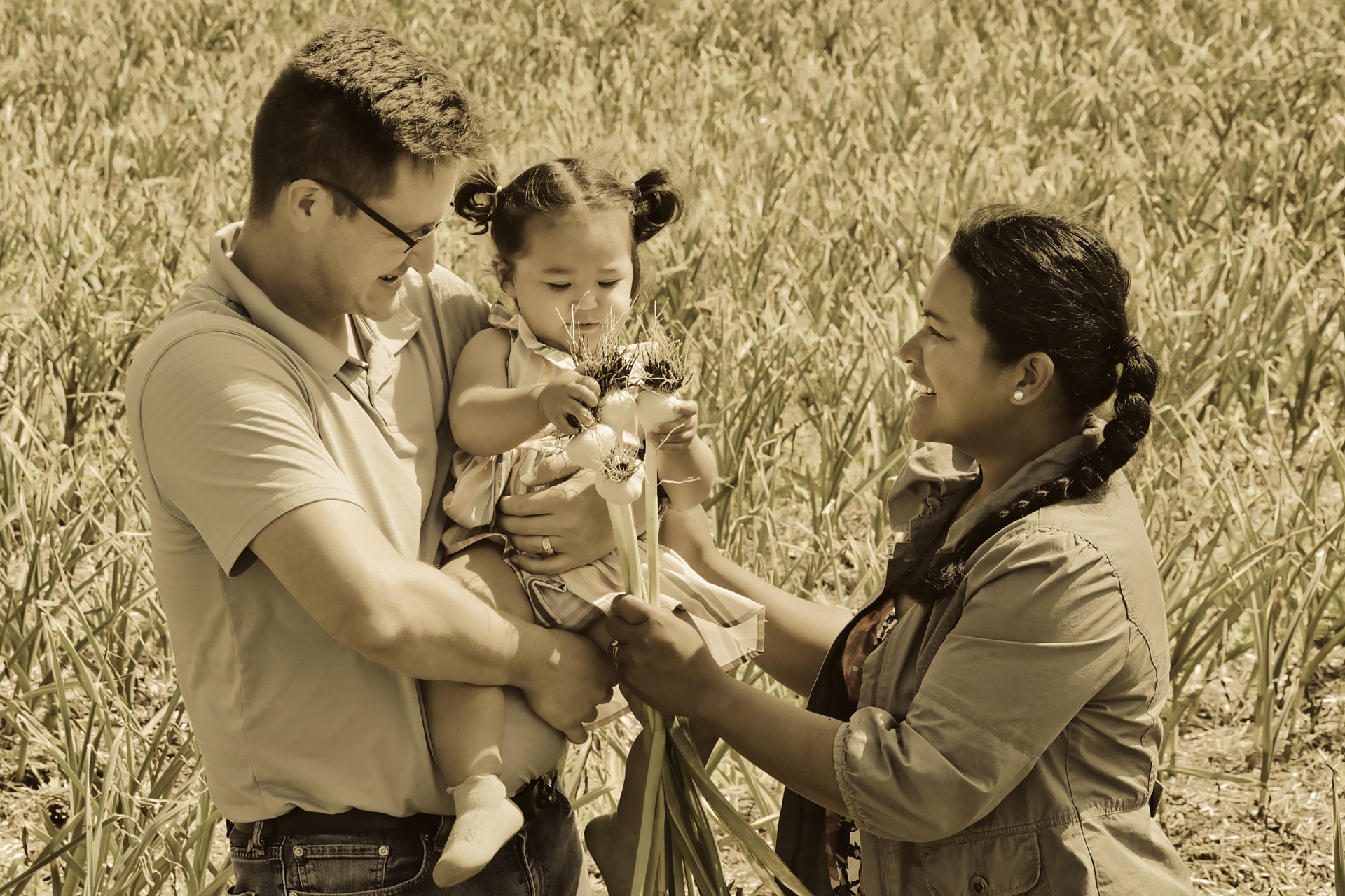 a man and woman holding a baby in a garlic field
