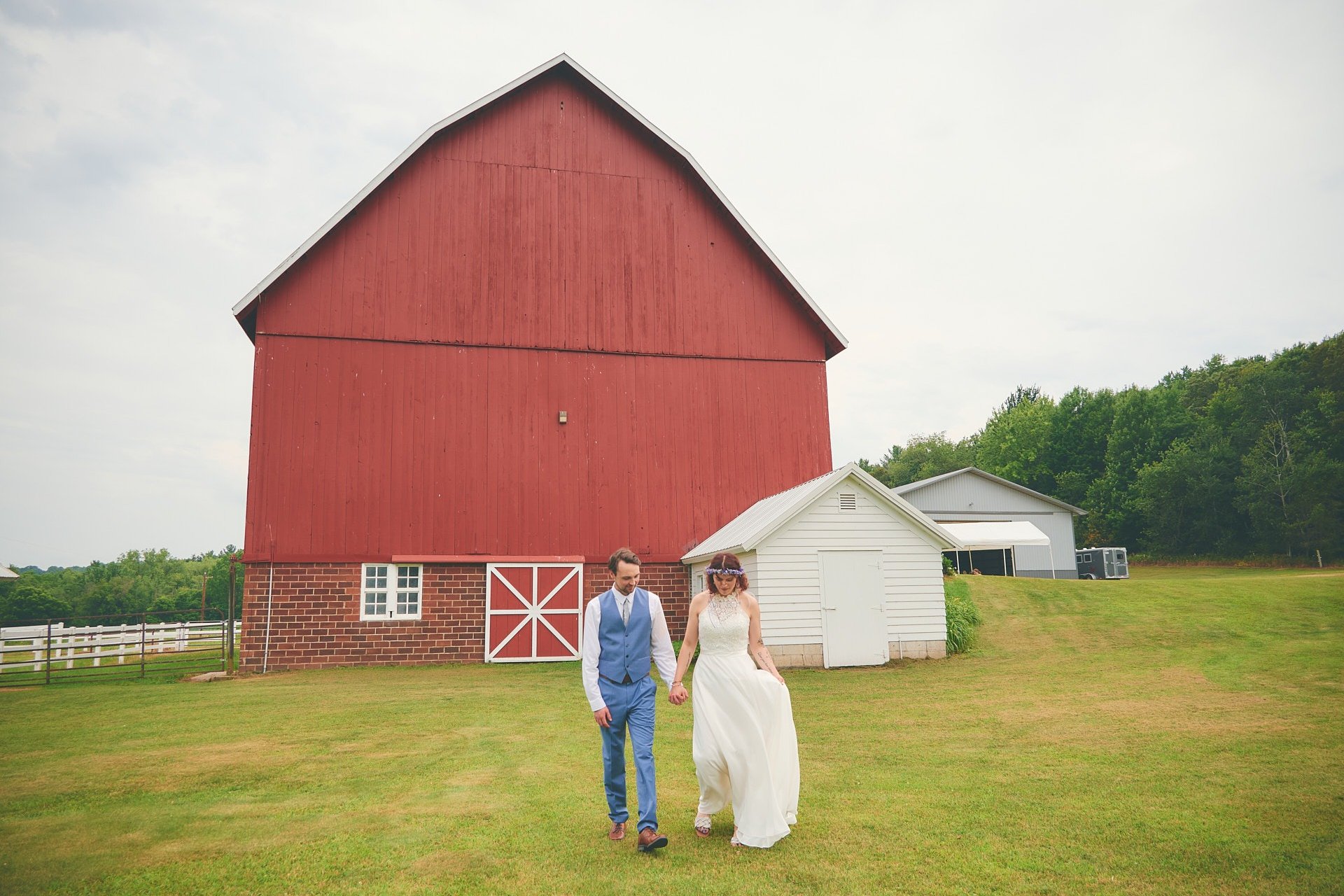 a bride and groom standing walking away from a barn
