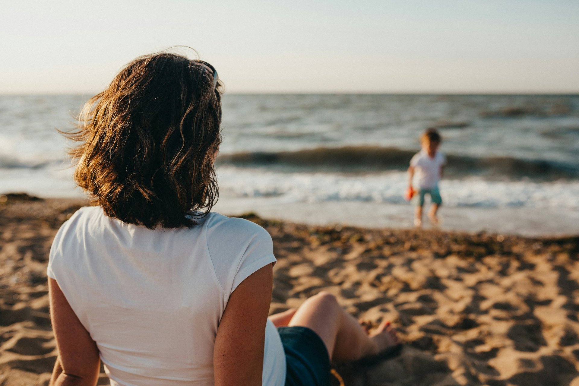 Mère assise sur la plage, face à la mer, regarde son fils jouer au bord de l'eau